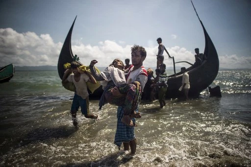 Sur cette photo d'archive prise le 30 septembre 2017, un homme bangladais aide des réfugiés musulmans rohingyas à débarquer d'un bateau sur la rive bangladaise de la rivière Naf après avoir traversé la frontière du Myanmar à Teknaf. (Fred Dufour /AFP)