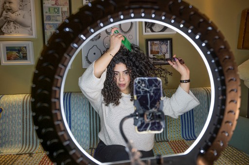 Mariam Ashraf, enseignante et «influenceuse des cheveux naturels», se coiffe en parlant devant un téléphone sur un trépied lors d'une diffusion en direct chez elle au Caire, le 22 mars 2022. (Khaled Desouki/AFP)