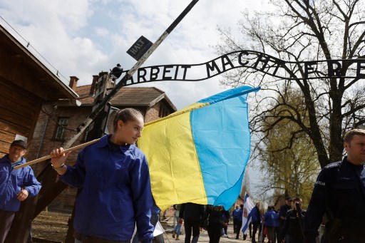 Viera de Vinnytsia en Ukraine pose avec le drapeau de son pays en marge des commémorations en l'honneur des victimes de l'Holocauste près de la porte principale de l'ancien camp d'Auschwitz-Birkenau. (Wojtek Radwanski/AFP)