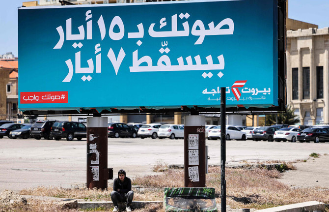 Un jeune assis sous un panneau d'affichage géant pour les prochaines élections législatives, avec un texte en arabe indiquant «votre vote le 15 mai annulera le 7 mai», sur la place des Martyrs, dans le centre de Beyrouth, la capitale du Liban, le 13 avril 2022. (AFP)