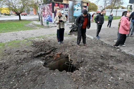 Des riverains observent un trou dans le trottoir d'un quartier résidentiel de la périphérie nord de Kharkiv après les bombardements du 22 avril 2022, alors que les pourparlers entre Moscou et Kiev pour mettre fin à la campagne militaire russe en Ukraine sont «au point mort», selon le ministre russe des Affaires étrangères. (Sergey Bobok / AFP)