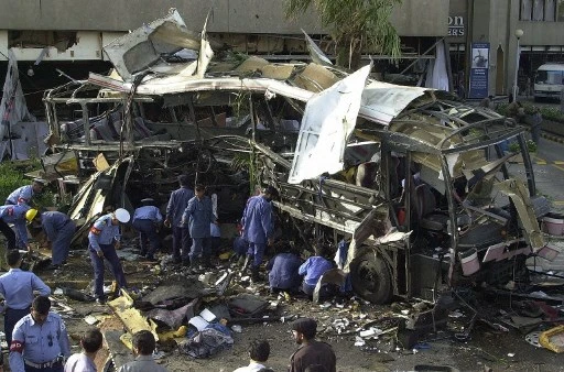 Dans cette photographie d'archives prise le 8 mai 2002, des responsables de la sécurité pakistanaise examinent l'épave d'un bus soufflé par un puissant attentat à la bombe devant l'hôtel Sheraton dans la ville portuaire de Karachi, qui a coûté la vie à 11 employés français. (Aamir Qureshi/AFP)