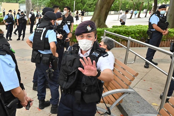 La police tente d'empêcher la prise de photos alors qu'elle interroge une femme (au centre, masquée) sur un banc du parc Victoria dans le quartier de Causeway Bay à Hong Kong le 4 juin 2022, le lieu où les Hongkongais se rassemblent traditionnellement pour pleurer les victimes de la répression de la place Tiananmen en Chine en 1989. (AFP)
