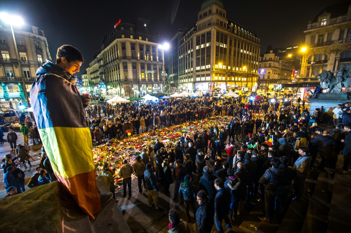 Sur cette photo d'archive prise le 24 mars 2016, un homme enveloppé dans un drapeau belge tient une bougie lors d’un rassemblement devant la Bourse de Bruxelles, deux jours après un triple attentat à la bombe, revendiqué par le groupe État islamique, qui a frappé l'aéroport de Bruxelles et la station de métro Maelbeek - Maalbeek, faisant 31 morts et 300 blessés. (Photo de Philippe Huguen / AFP)