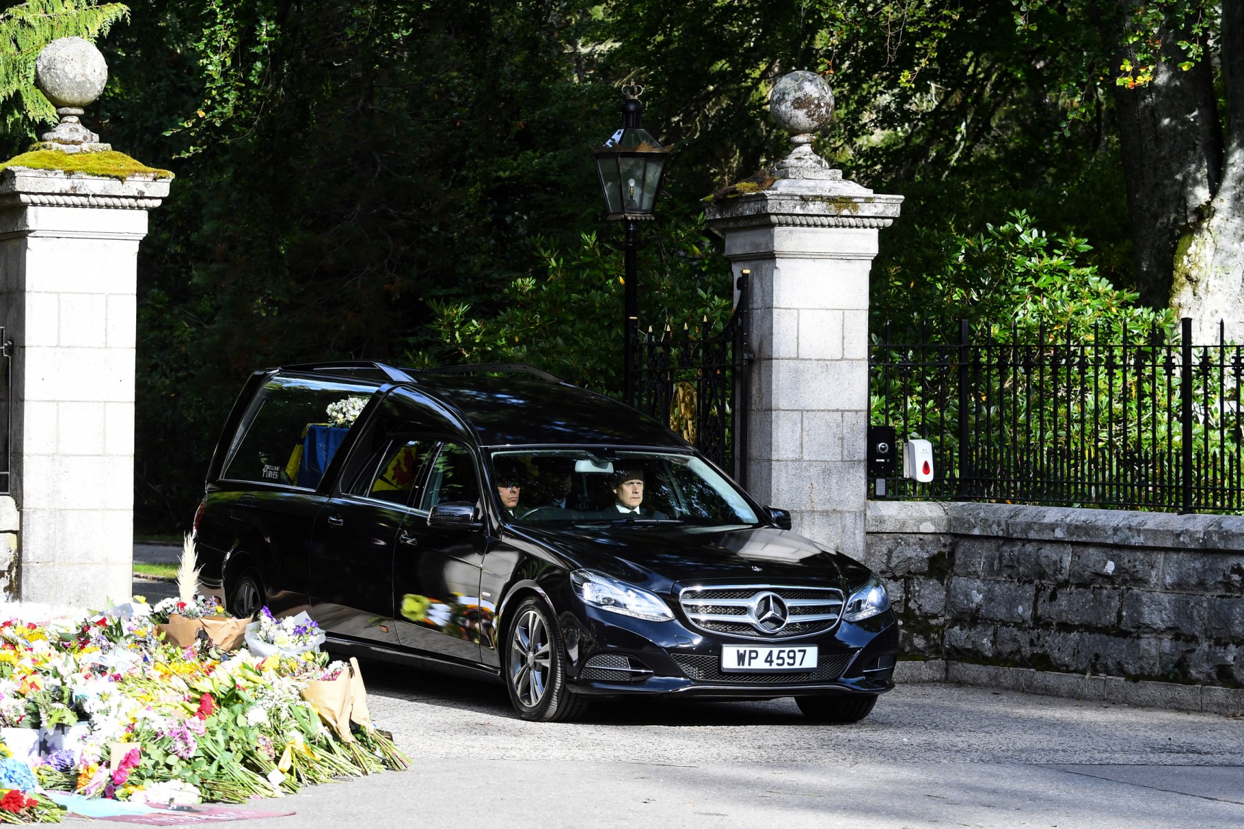 Le corbillard transportant le cercueil de la Reine Elizabeth II recouvert de l'étendard royal d'Écosse et d'une fleur s'éloigne du château de Balmoral à Ballater, le 11 septembre 2022. Le cercueil de la reine Élisabeth II traversera les villes et villages écossais dimanche, alors qu'il entamera son dernier voyage depuis sa chère retraite écossaise de Balmoral. La reine, décédée le 8 septembre, sera conduite au palais de Holyrood House avant de reposer dans la cathédrale St Giles, puis de se rendre à Londres pour ses funérailles. (Photo : ANDY BUCHANAN / AFP)