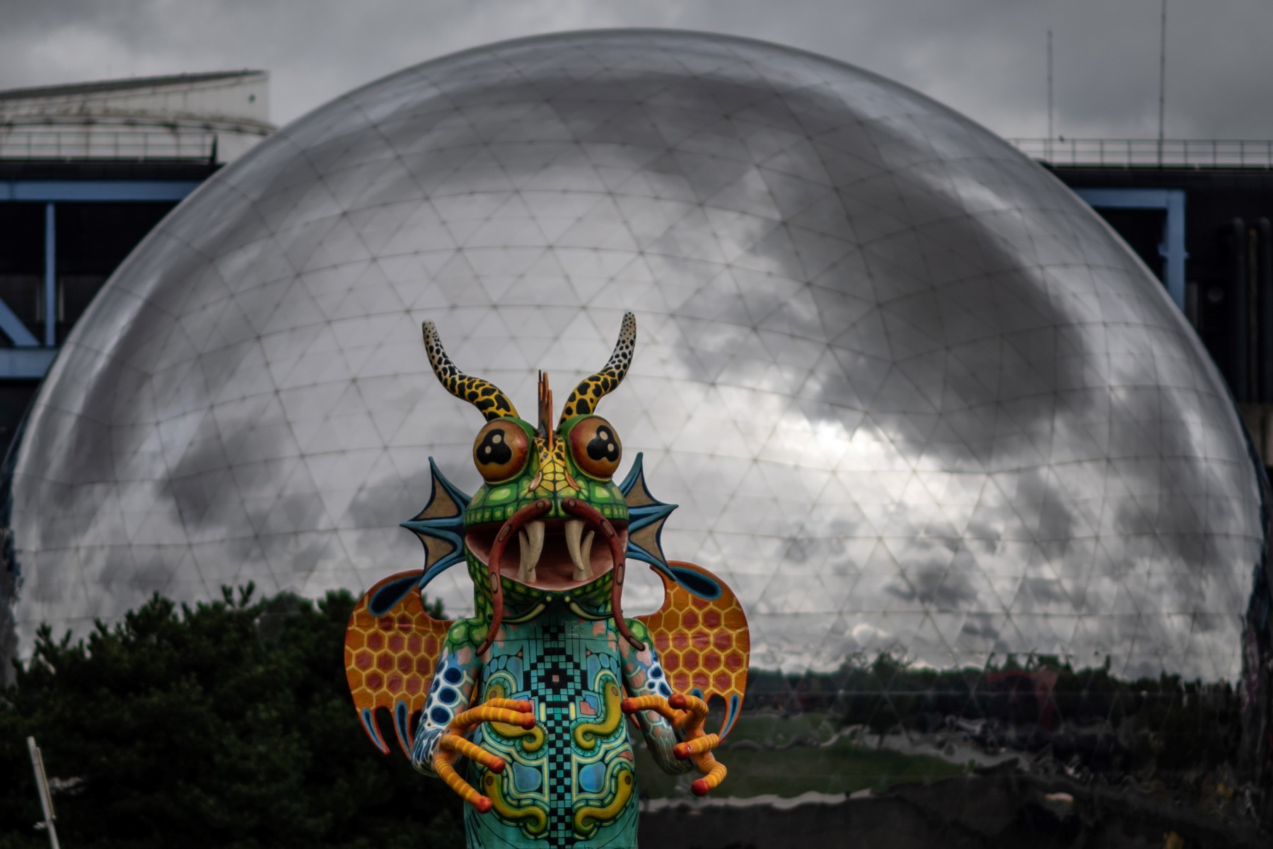 Une statue mexicaine Alebrijes est exposée au bord du canal de l'Ourq, la "Géode", une sphère en acier abritant une salle de projection à la Cité des Sciences et de l'Industrie, dans le parc de la Villette à Paris, le 10 juillet 2020. (photo, AFP / Martin BUREAU)