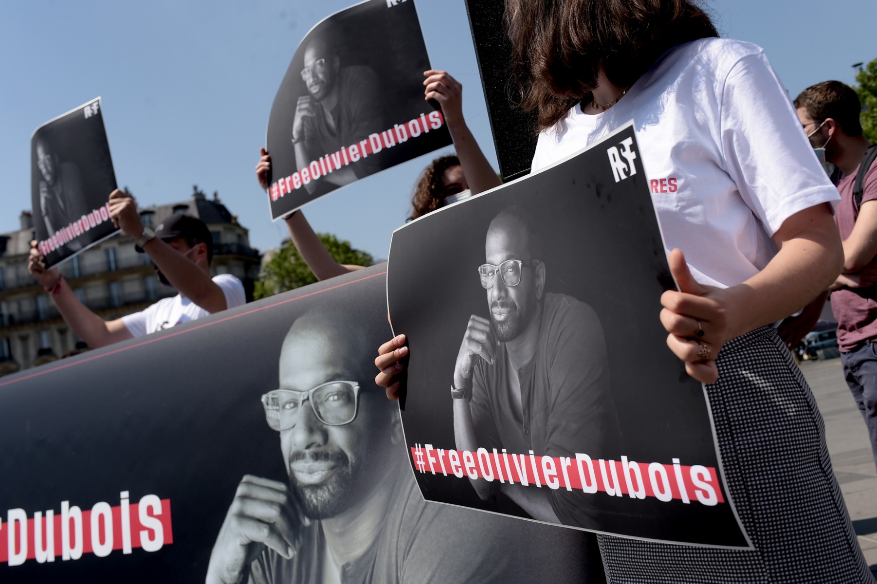 Des personnes tiennent une pancarte avec un portrait du journaliste français Olivier Dubois à Paris, le 8 juin 2021, lors d'un rassemblement de soutien après son enlèvement dans le nord du Mali en avril par un groupe djihadiste lié à Al-Qaïda. (Lucas Barioulet, AFP)