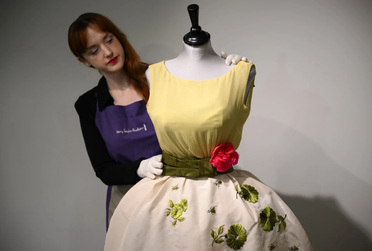 Un employé pose avec une robe Christian Dior portée par l'actrice Elizabeth Taylor, et récemment découverte avec d'autres robes dans une valise, avant leur vente chez Kerry Taylor Auctions, à Londres, le 25 novembre 2022. (Photo de Daniel LEAL / AFP)