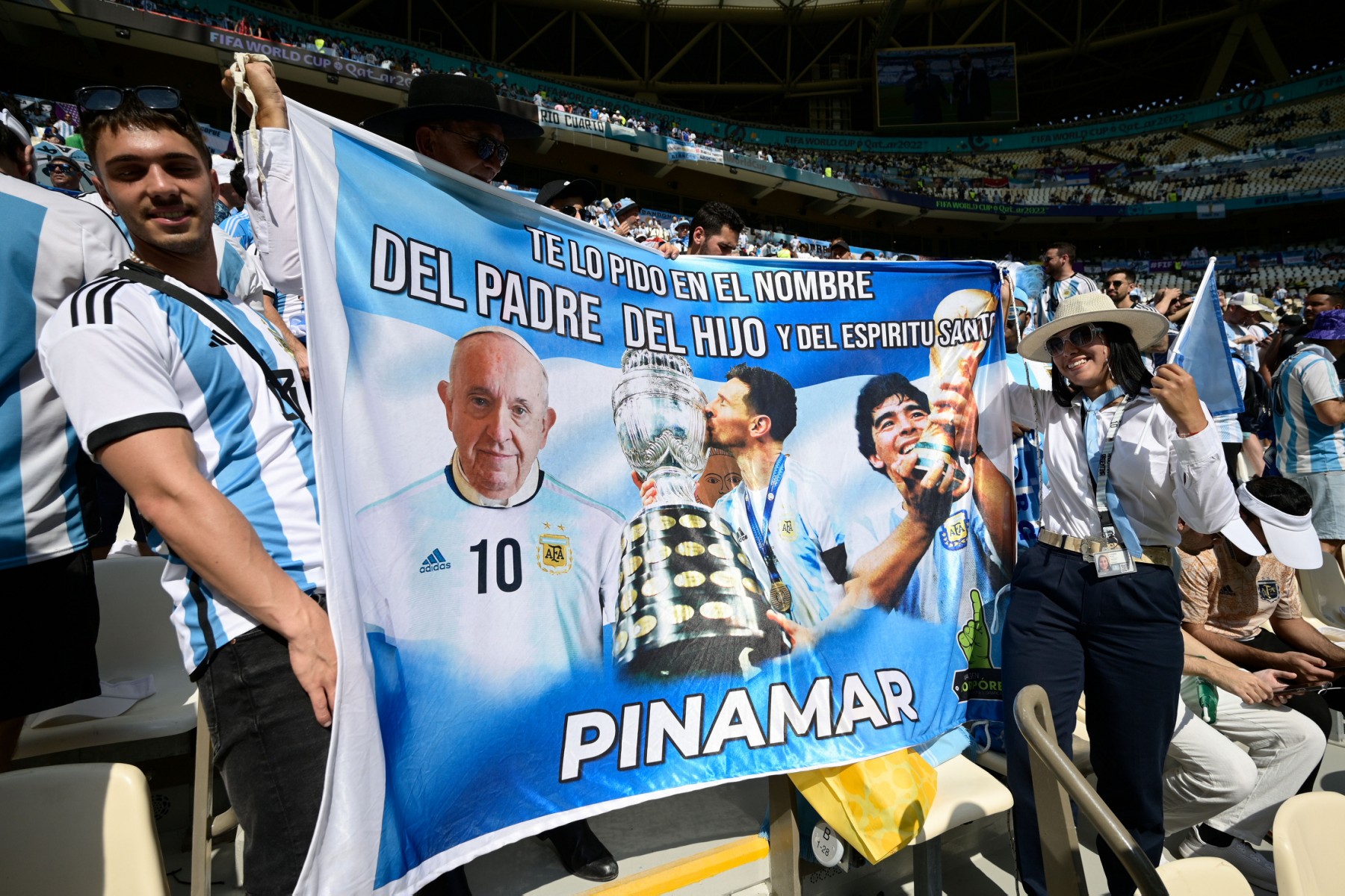 Des supporters argentins agitent un drapeau représentant le pape François, l'attaquant argentin n°10 Lionel Messi et la légende du football Diego Maradona avant le début du match de football du groupe C de la Coupe du monde Qatar 2022 entre l'Argentine et l'Arabie saoudite au stade Lusail, à Doha, le 22 novembre 2022. (Photo par Juan Mabromata / AFP)
