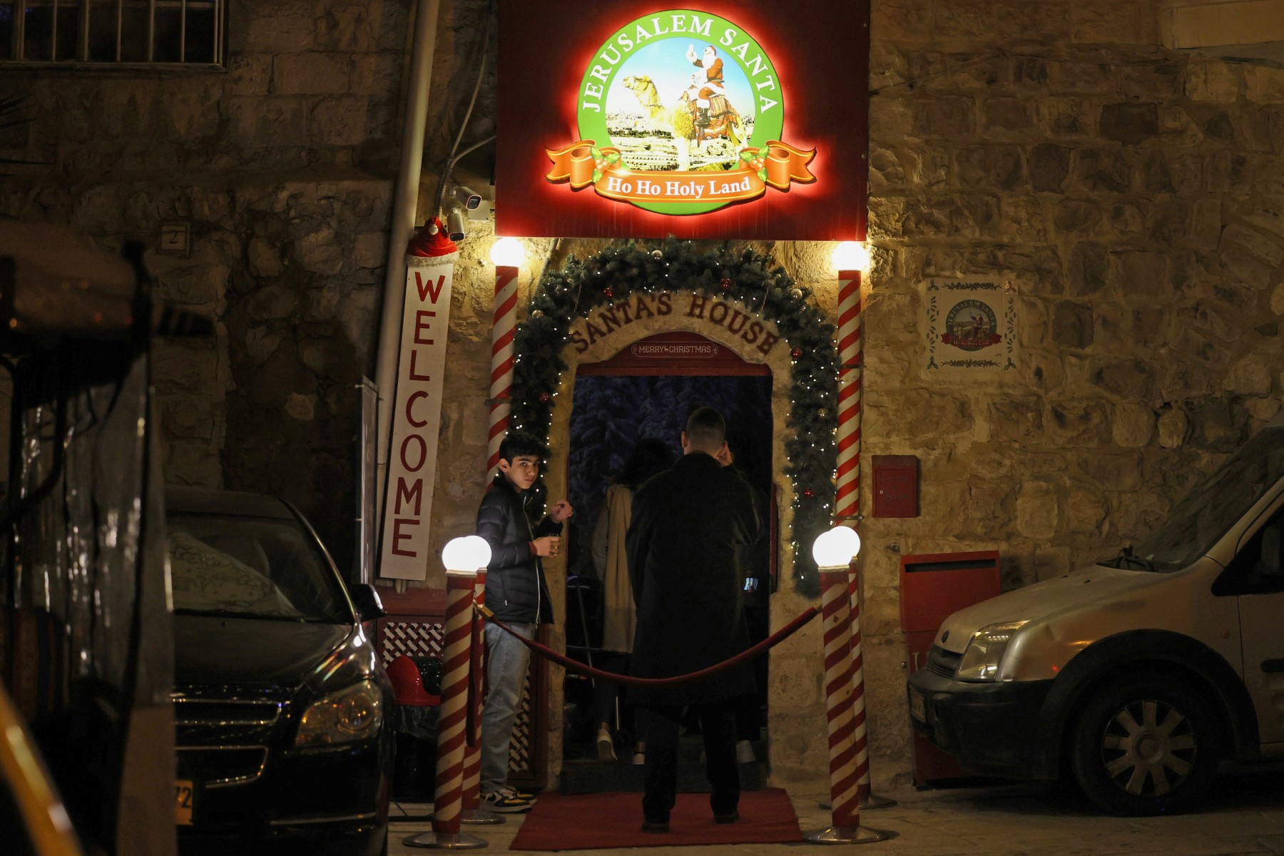 Des visiteurs entrent dans la maison du Père Noël au rez-de-chaussée de la maison du Palestinien Issa Kassissieh (invisible) qui les accueille en tant que Père Noël, dans la vieille ville de Jérusalem, quelques semaines avant la fête de Noël, le 1er décembre 2022. (Photo par Ahmad Gharabli / AFP)