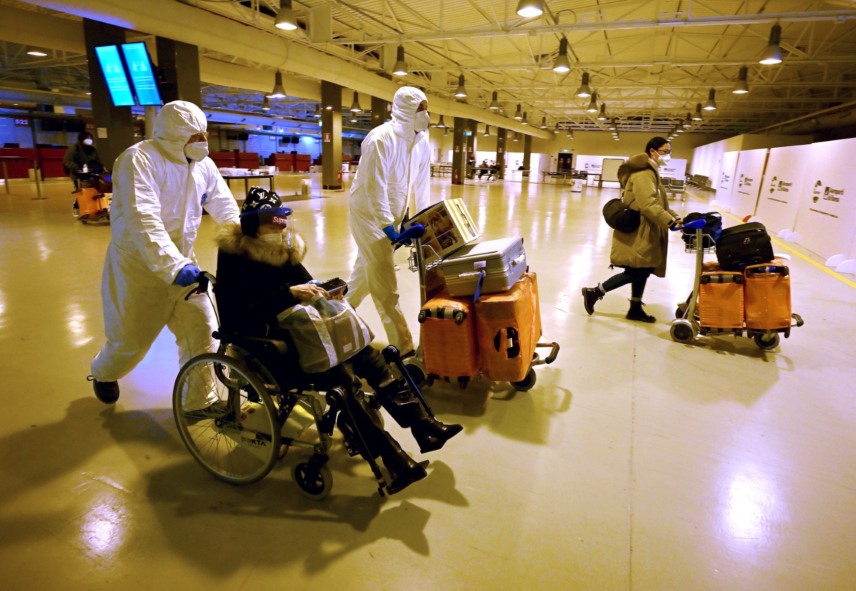 Des travailleurs portant des masques et des combinaisons de protection aident des voyageurs chinois à quitter le hall d'arrivée de l'aéroport international de Rome-Fiumicino, près de Rome, le 29 décembre 2022, après avoir été testés pour le coronavirus Covid-19. (Photo de Filippo Monteforte / AFP)