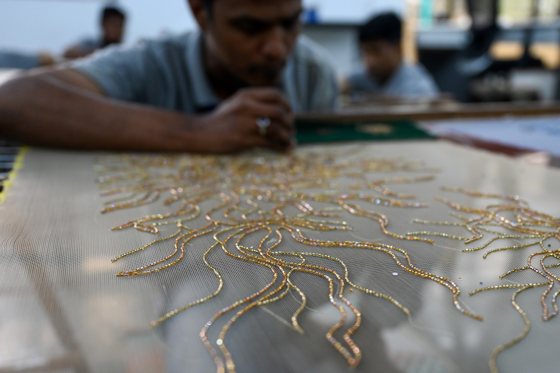 Sur cette photo prise le 7 janvier 2023, un brodeur de Shanagar, un atelier de broderie manuelle de luxe basé à Mumbai, travaille sur un modèle pour le couturier français Julien Fournié, dans une unité de production à Mumbai. (Photo de Punit PARANJPE / AFP)