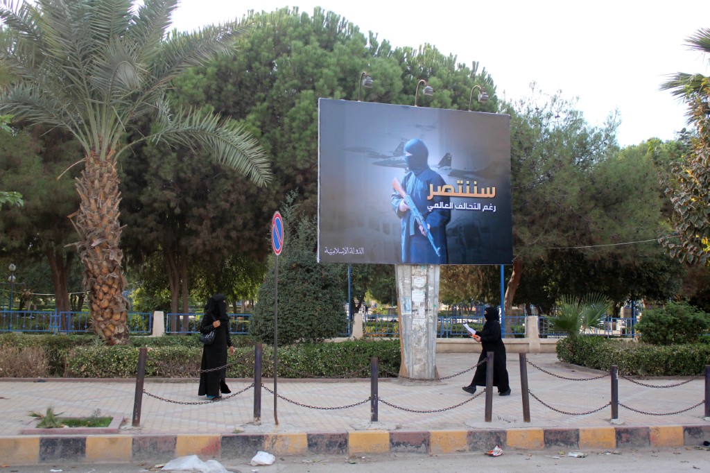 Des femmes portant un niqab, marchent sous un panneau publicitaire érigé par le groupe État islamique (EI) dans le cadre d'une campagne dans la ville syrienne de Raqqa, contrôlée par l'EI, le 1er novembre 2014. (Photo par Raqa Media Center / AFP)