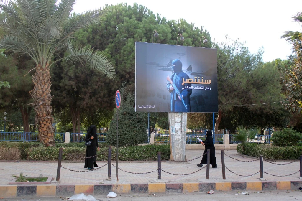 Des femmes portant un niqab, marchent sous un panneau publicitaire érigé par le groupe État islamique (EI) dans le cadre d'une campagne dans la ville syrienne de Raqqa, contrôlée par l'EI, le 1er novembre 2014. (Photo par Raqa Media Center / AFP)