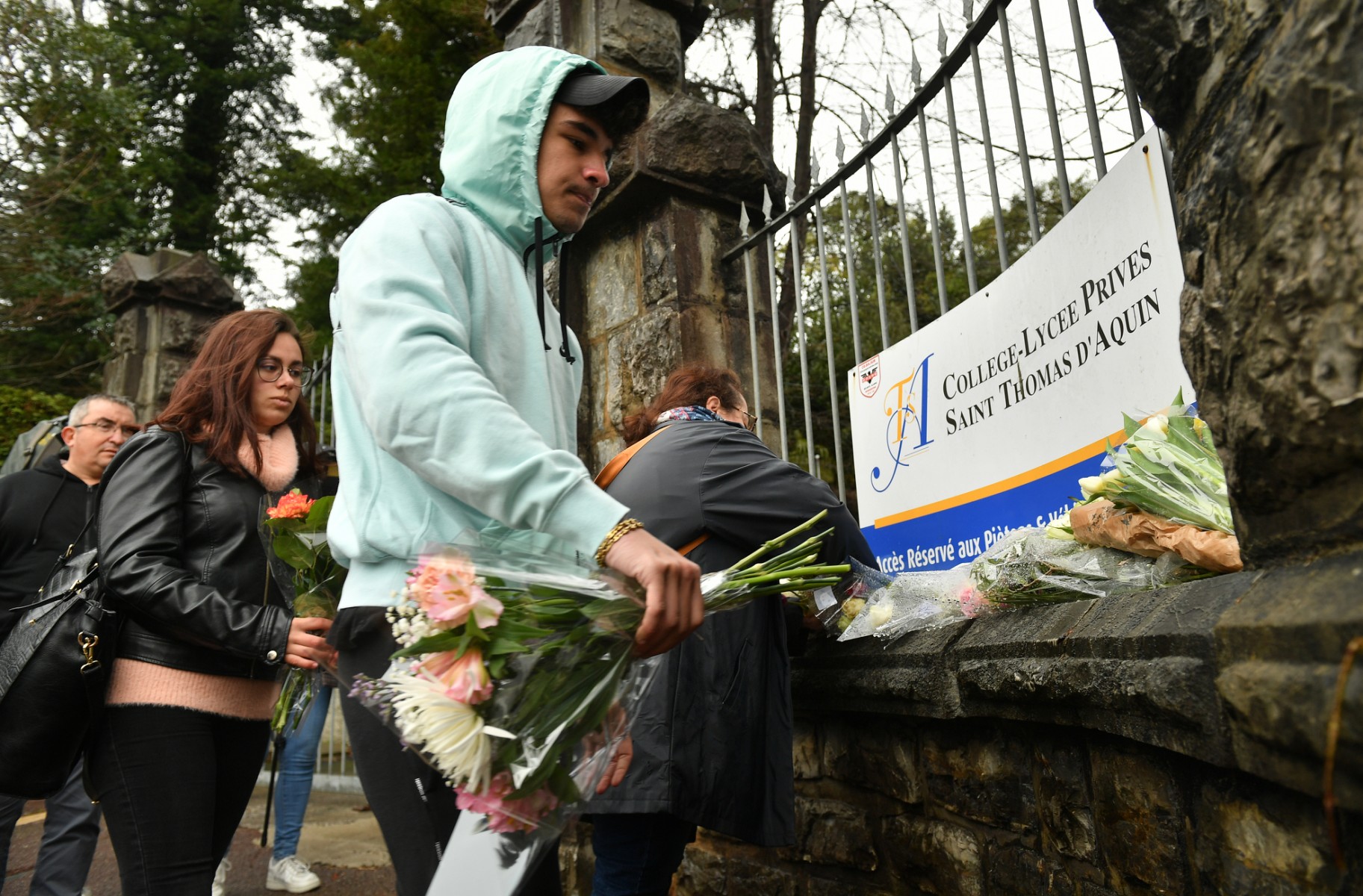 Des personnes déposent des bouquets de fleurs devant le portail d'entrée du collège Saint-Thomas d'Aquin où une enseignante est morte après avoir été poignardée par un élève, à Saint-Jean-de-Luz, dans le sud-ouest de la France, le 23 février 2023. (Photo de Gaizka Iroz / AFP)