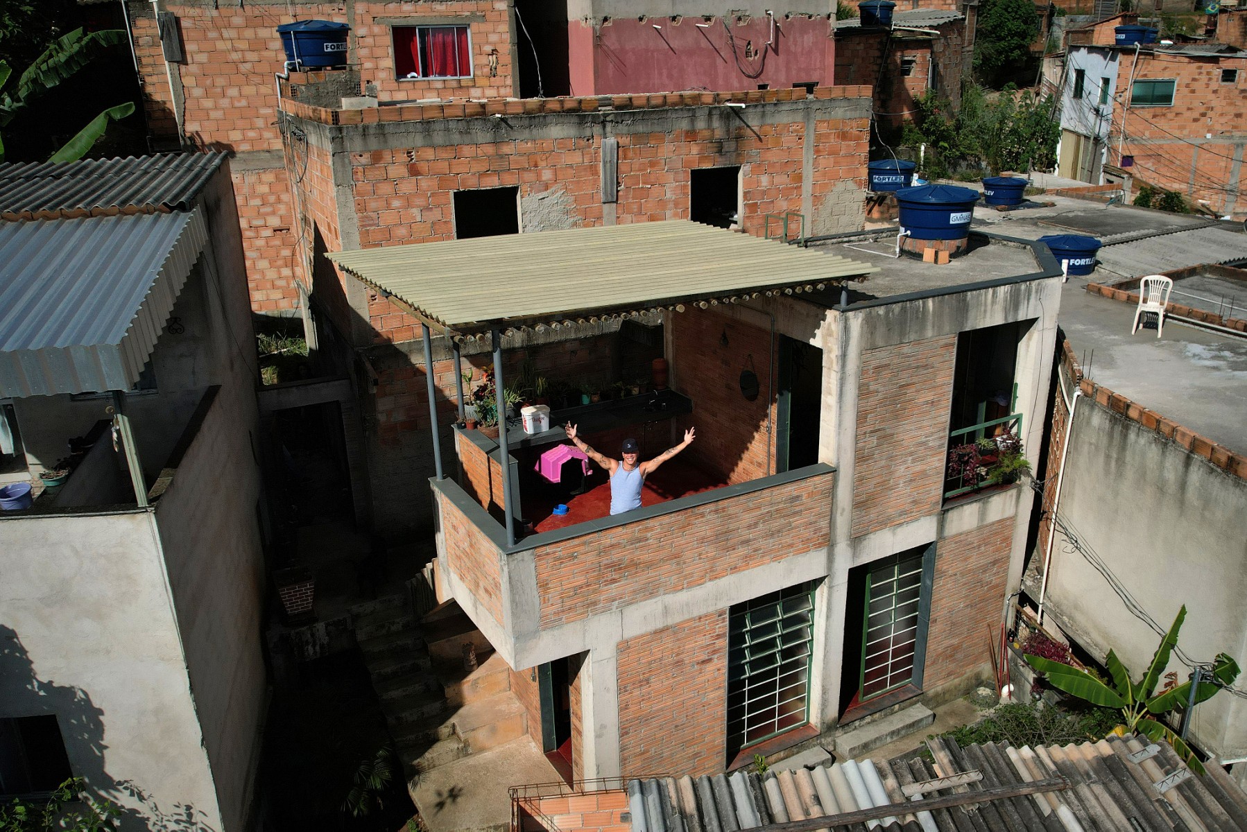 Vue aérienne montrant l'artiste musical brésilien Kdu dos Anjos faisant des gestes devant sa maison, désignée "Bâtiment de l'année 2023" par le site de référence spécialisé ArchDaily, à Aglomerado da Serra, un complexe de favelas situé à la périphérie de Belo Horizonte, dans l'État du Minas Gerais, au Brésil, le 24 février 2023. (Photo de Douglas Magno / AFP)