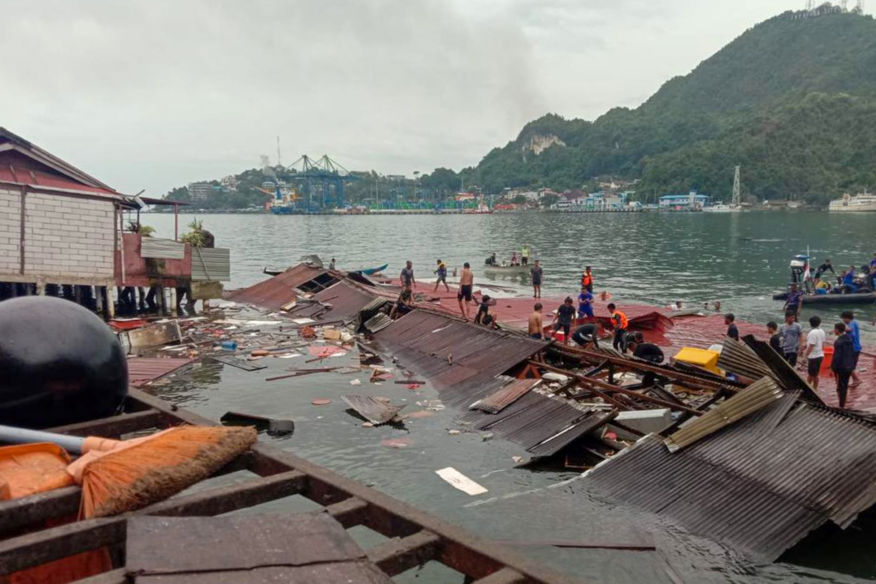 Des personnes se tiennent sur les toits des magasins effondrés dans le port après un tremblement de terre de magnitude 5,1 à Jayapura, dans la province orientale de Papouasie en Indonésie, le 9 février 2023. (Photo par Faisal Narwawan / AFP)