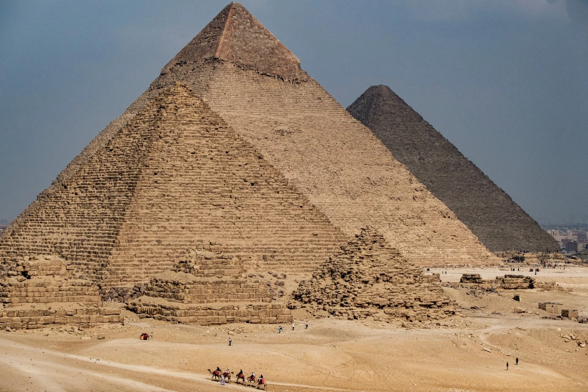 Des personnes montent des chameaux près de la pyramide de Menkaure (Menkheres), de la pyramide de Khafre (Chephren) et de la grande pyramide de Khufu (Cheops) dans la nécropole des pyramides de Gizeh, à la périphérie de la ville jumelle du Caire, capitale de l'Égypte, le 4 novembre 2022. (Photo Amir Makar / AFP)