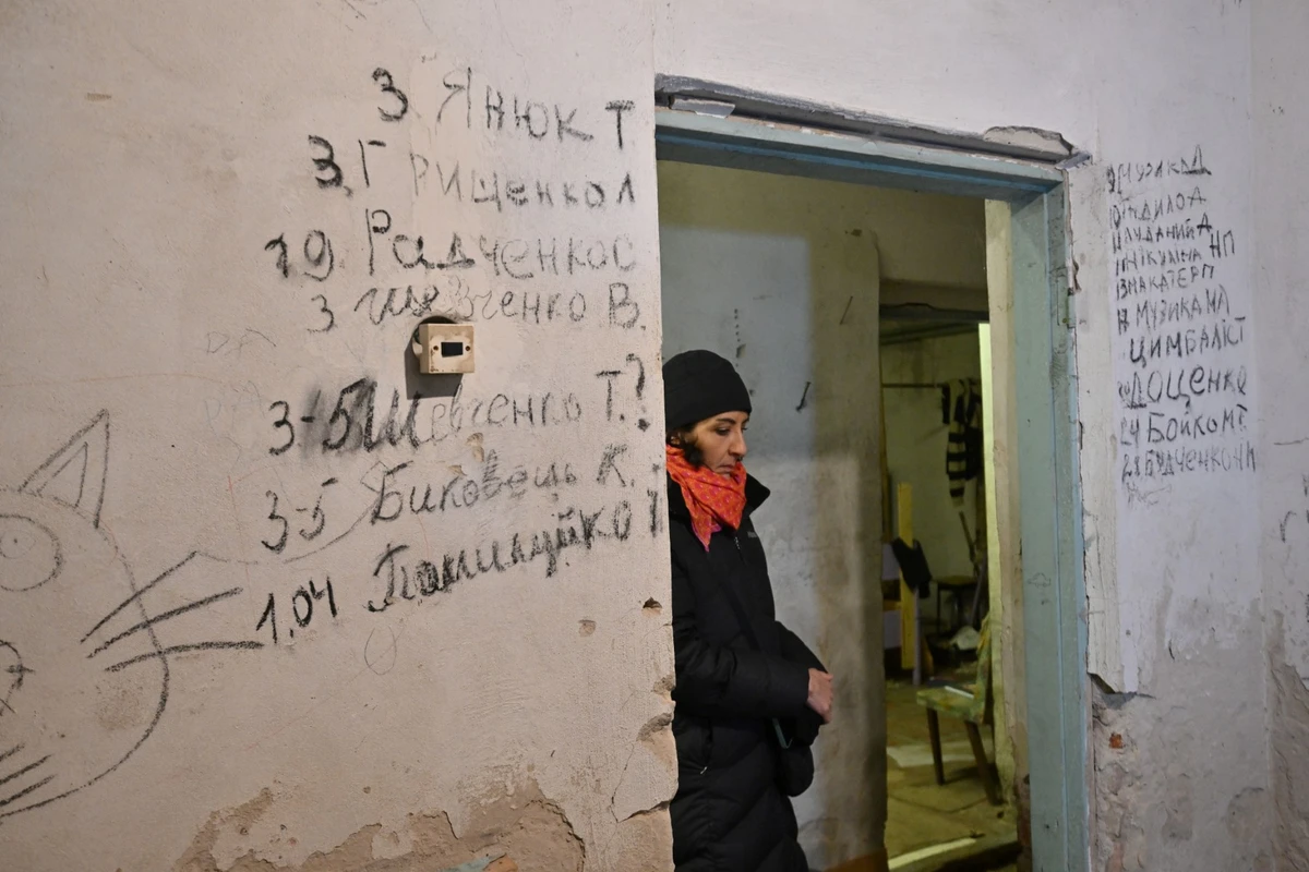 Un visiteur se tient à côté de la liste des noms des villageois décédés dans le sous-sol d'une école où ils ont été enfermés pendant près d'un mois par les troupes russes dans le village de Yagidne, au nord de Kiev, un an après la libération de la localité, le 3 avril 2023, lors de l'invasion russe de l'Ukraine. (Photo de Sergei Supinsky / AFP)