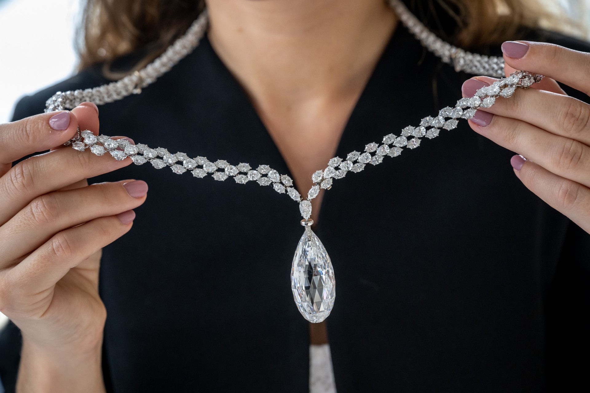 Cette photographie prise le 8 mai 2023 montre un employé de la maison de vente aux enchères Christie's tenant la "Briolette of India", un diamant incolore (D) de 90,36 carats, un collier de diamants qui devrait rapporter au moins 10 millions USD lors de la vente "World of Heidi Horten" à Genève. (Photo de Fabrice COFFRINI / AFP)