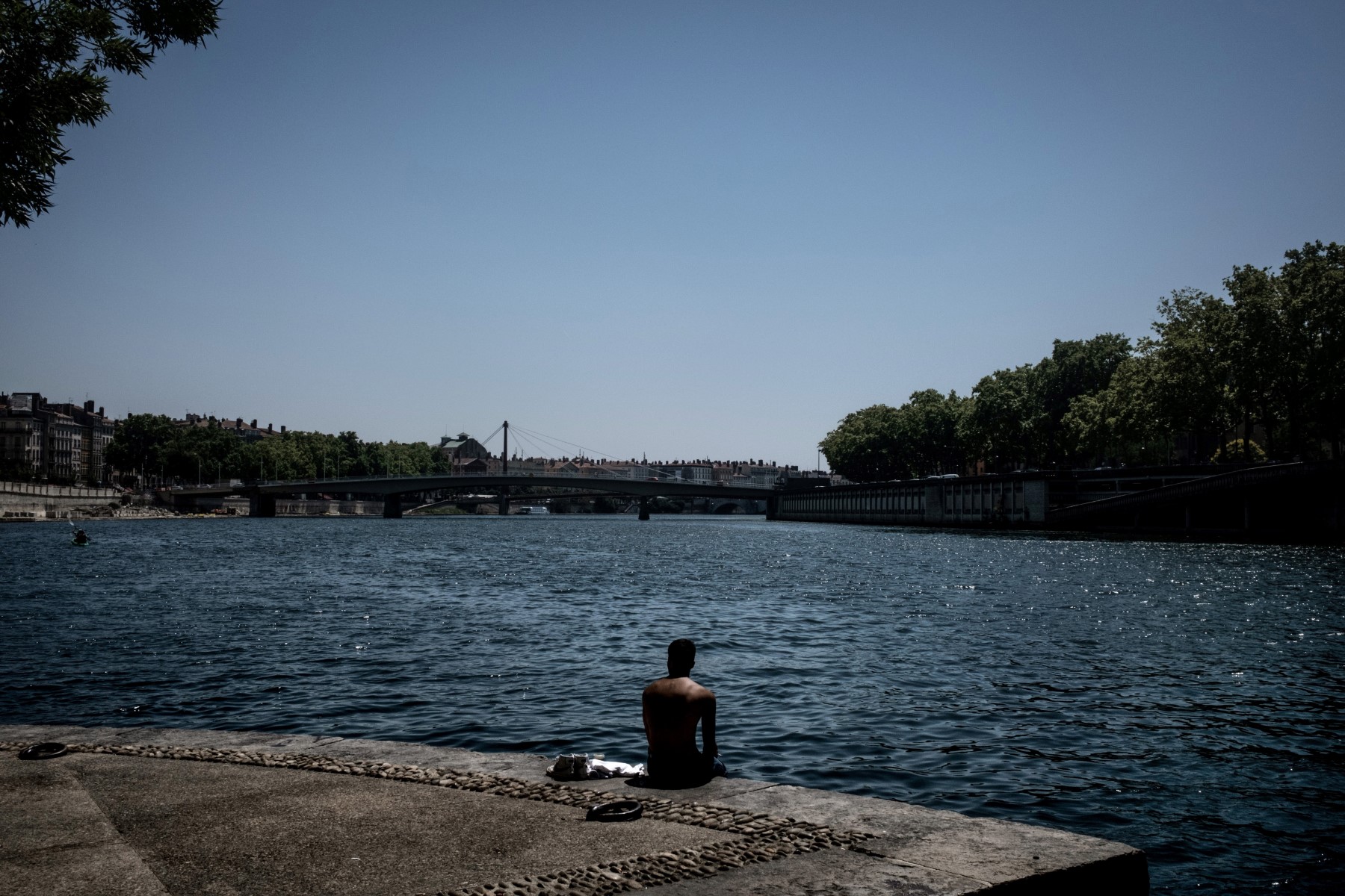 Une personne assise sur les quais de la Saône, alors qu'une vague de chaleur frappe la France, à Lyon, le 18 juin 2022. (Photo JEFF PACHOUD / AFP)