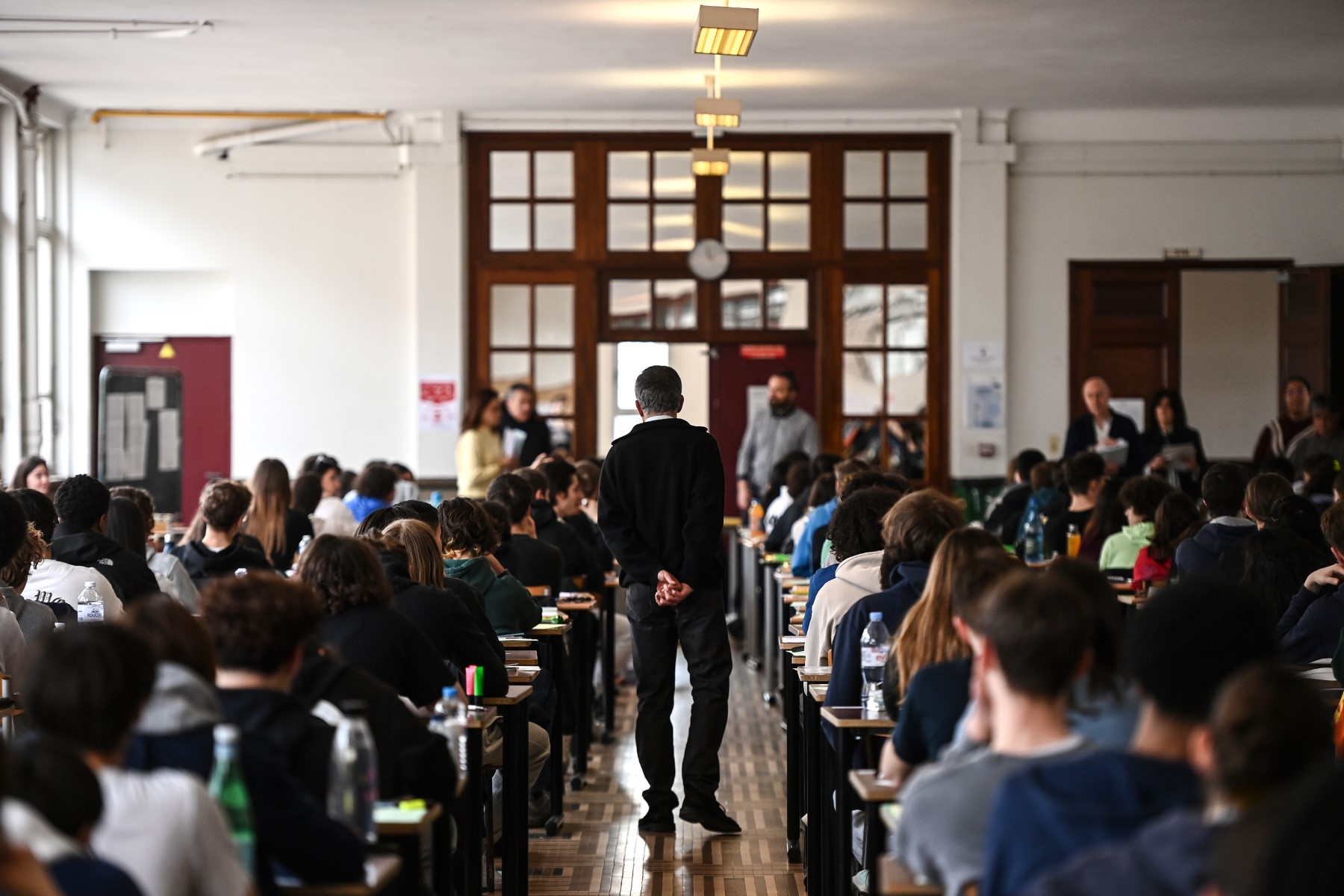 Un surveillant traverse des rangées de tables alors que des élèves se préparent avant de passer une épreuve dans le cadre des "epreuves de specialite du baccalaureat", à Paris, le 20 mars 2023. (Photo Christophe ARCHAMBAULT / AFP