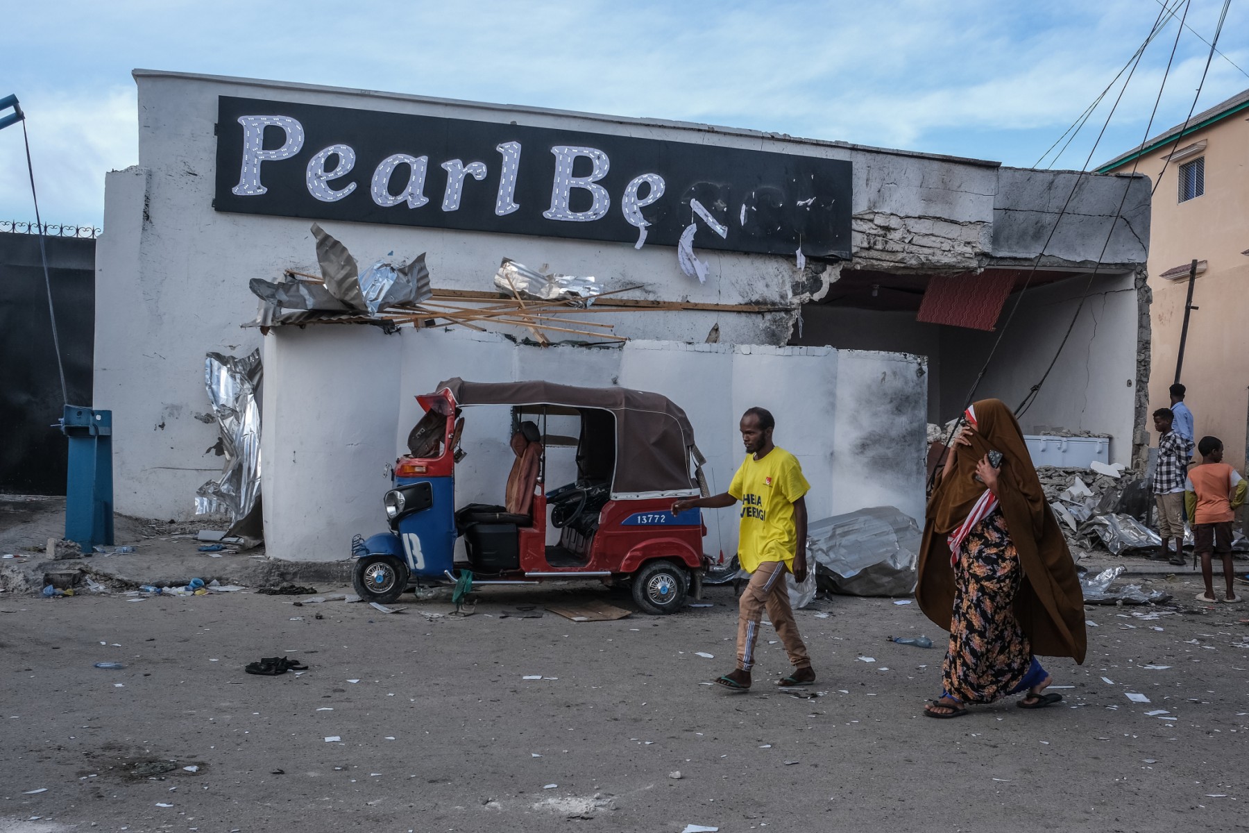Des habitants passent devant un tuk-tuk endommagé laissé à l'extérieur du site de l'attaque de l'hôtel Palm Beach à Mogadiscio, le 10 juin 2023. (Photo Hassan Ali ELMI / AFP)