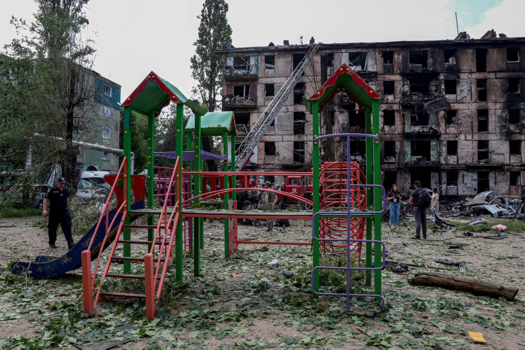 Un policier passe devant une aire de jeux pour enfants et un immeuble résidentiel détruit à la suite d'une attaque russe, dans la ville de Kryvyi Rig, le 13 juin 2023, dans le contexte de l'invasion russe de l'Ukraine. (Photo de Stas Yurchenko / AFP)