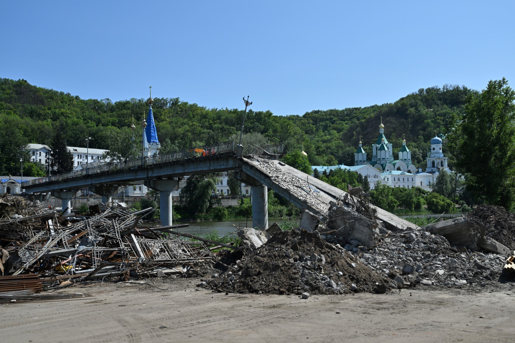 Des ouvriers nettoient les débris du pont détruit à côté du monastère chrétien orthodoxe de Svyatogirsk dans la ville de Svyatogirsk, dans la région de Donetsk, le 22 juin 2023, lors de l'invasion russe de l'Ukraine. (Photo de Genya SAVILOV / AFP)
