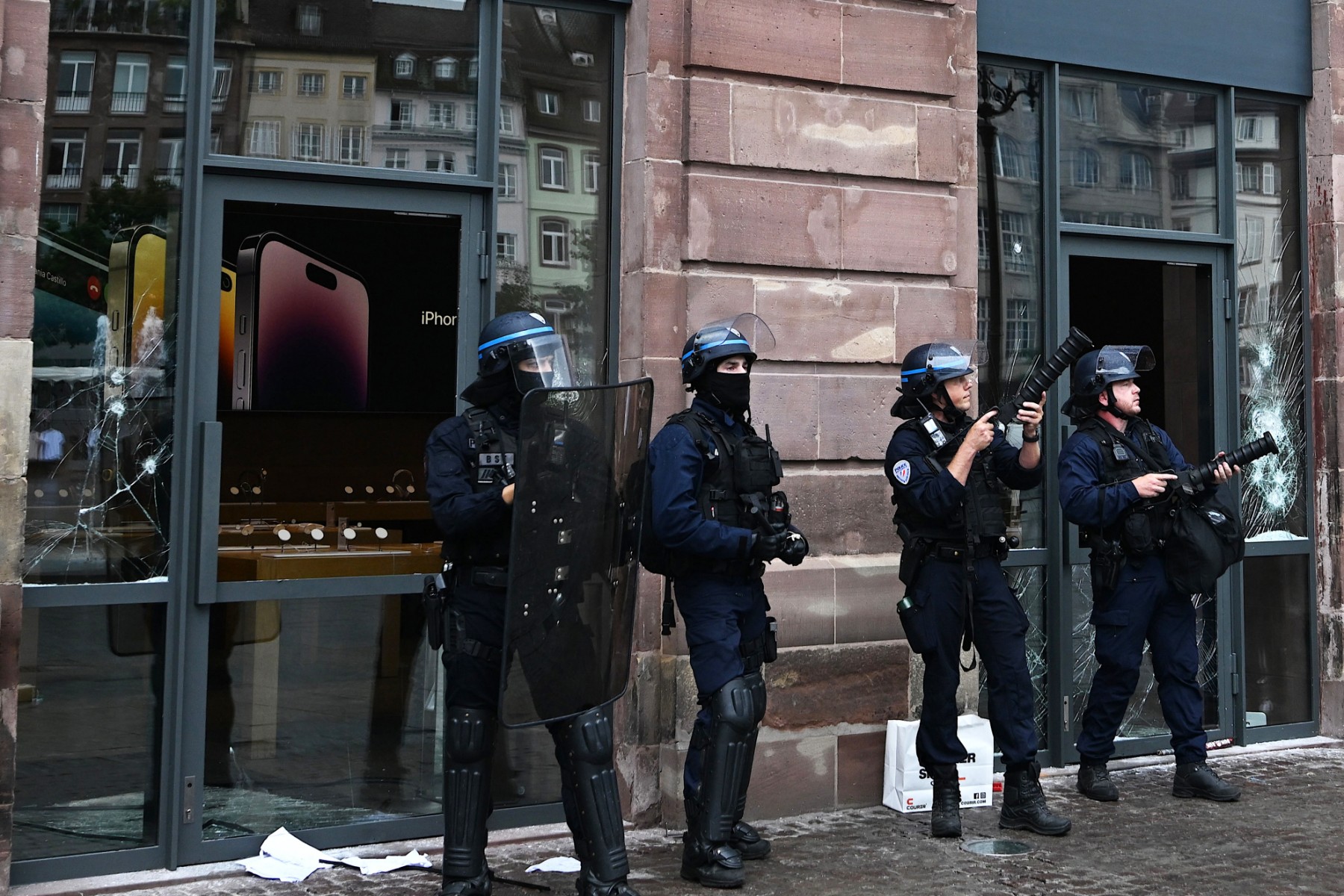 Des policiers français en tenue anti-émeute montent la garde et tiennent des lanceurs de grenades lacrymogènes à côté de la façade d'un Apple Store endommagé place Kleber, à Strasbourg, dans l'est de la France, le 30 juin 2023. (Photo by PATRICK HERTZOG / AFP)