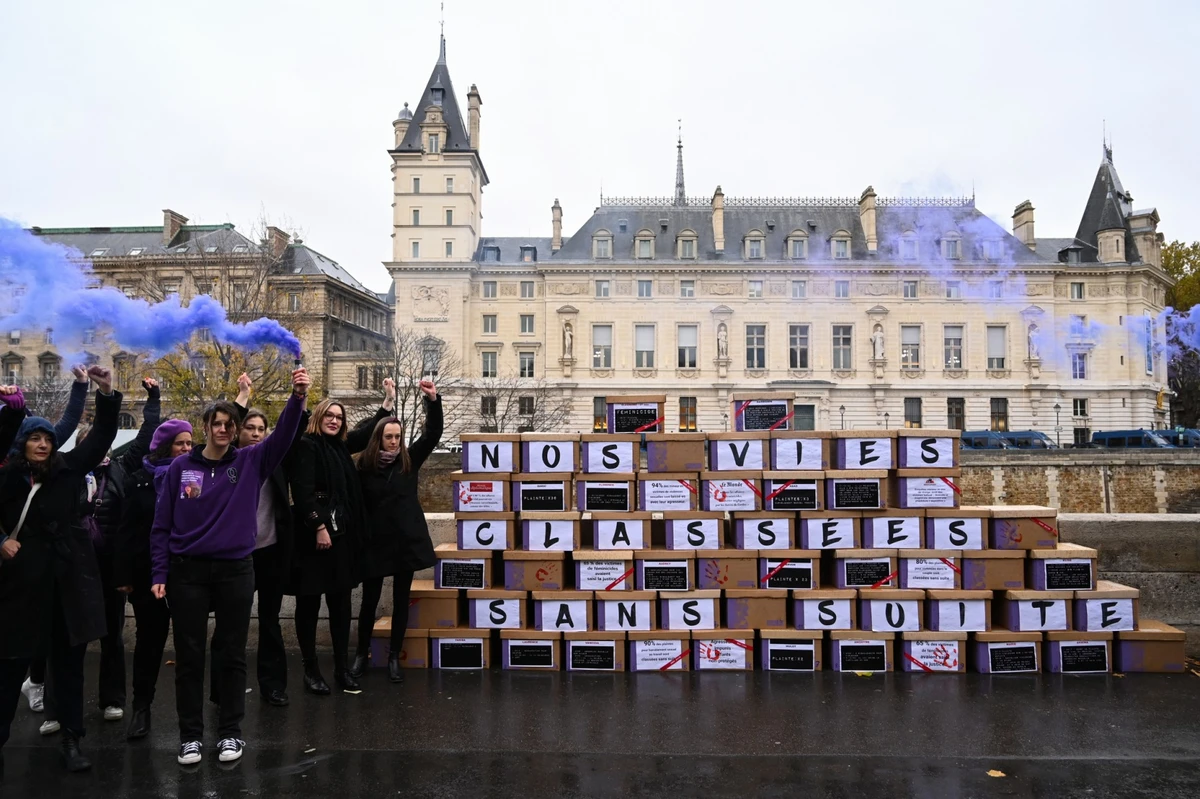 Des manifestants brandissent une fusée violette à côté d'un mur composé de cartons de dossiers, pour symboliser les dossiers classés sans suite, devant le Palais de Justice, le palais historique situé sur l'Ile de la Cité à Paris, le 23 novembre 2022. (Photo par Bertrand GUAY / AFP)