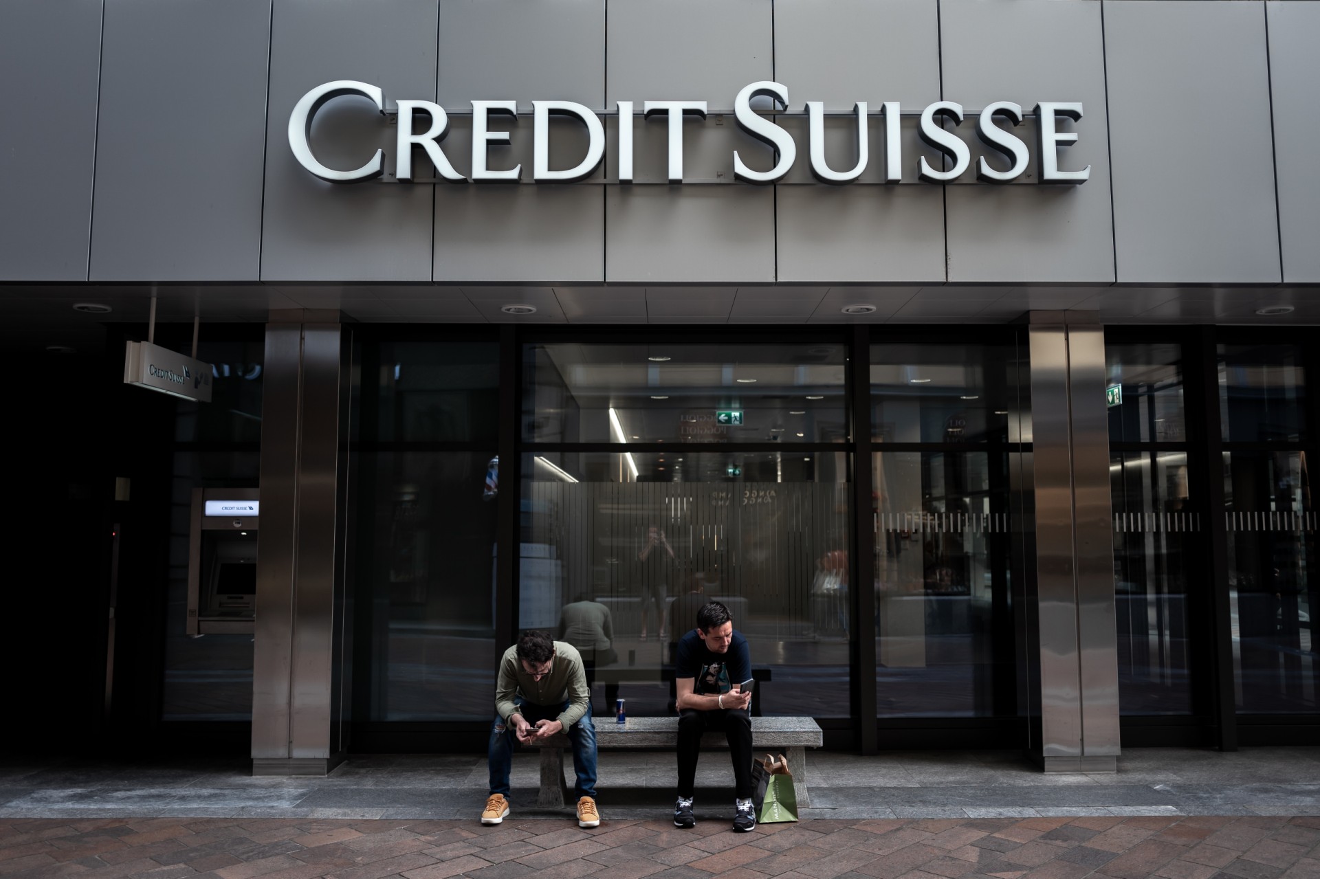 Deux hommes assis sous un panneau du Credit Suisse affiché sur un bâtiment à Lugano, le 9 juin 2023. (Photo de Fabrice Coffrini / AFP)