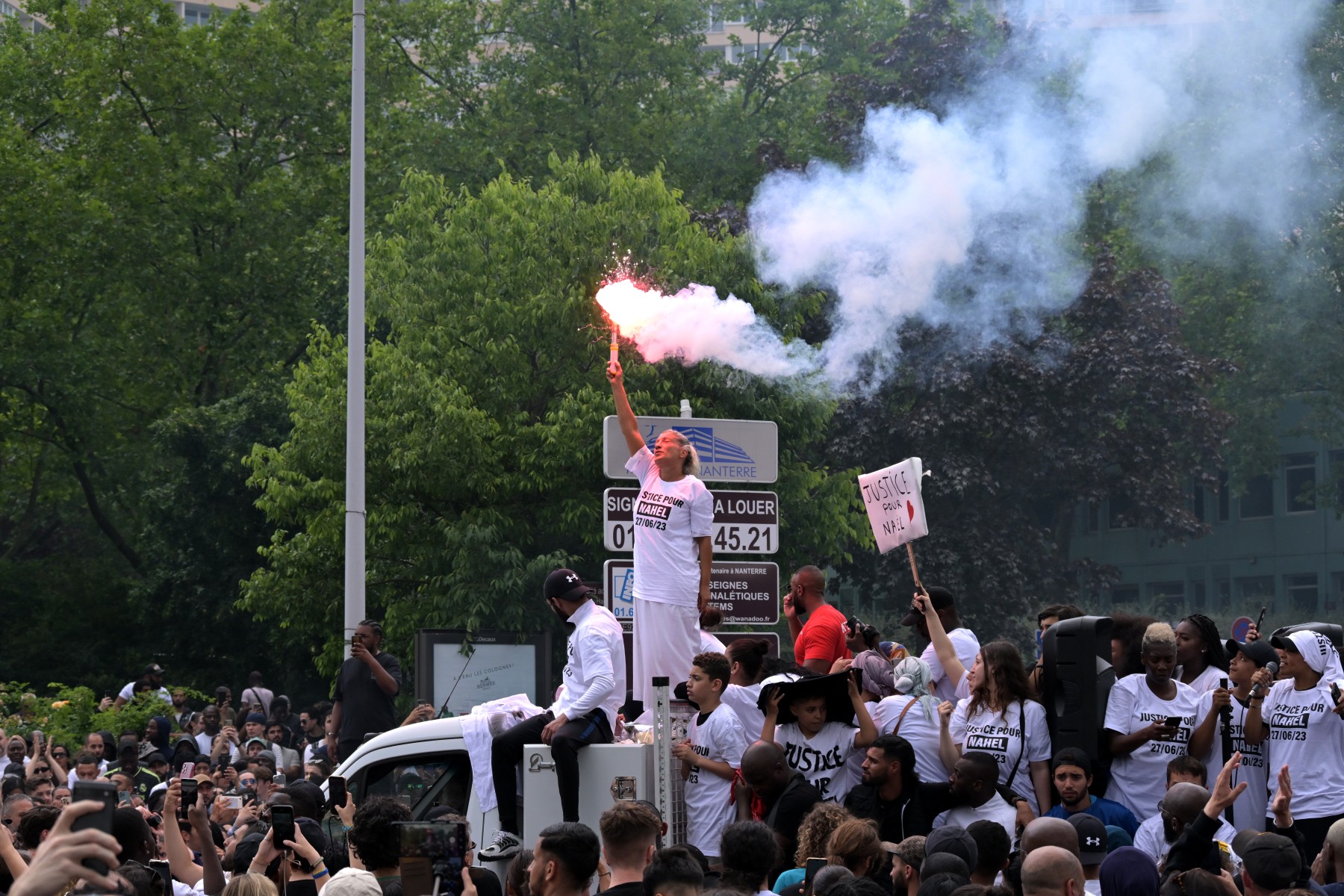 Mounia, la mère de Nahel, un adolescent abattu par un policier, agite une fusée éclairante alors qu'elle se tient debout sur un camion lors d'une marche commémorative pour son fils, dans la banlieue parisienne de Nanterre, le 29 juin 2023. (Photo par Alain JOCARD / AFP)