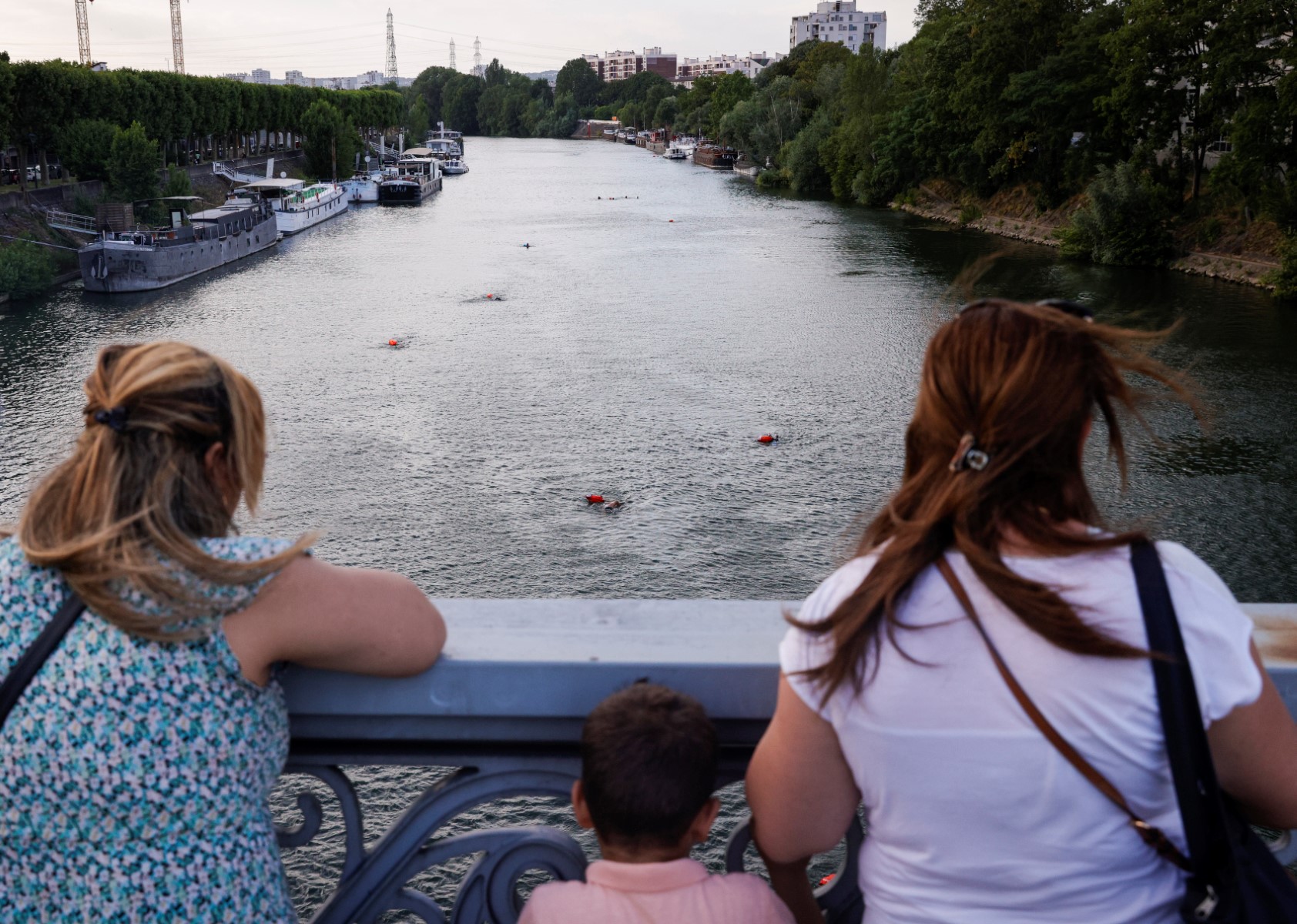Des membres du public regardent depuis un pont un groupe de personnes nageant dans la Seine depuis un bateau à l'Ile-Saint-Denis, au nord de Paris, le 2 juillet 2023. Il est toujours interdit de se baigner dans la Seine, mais à un an des Jeux Olympiques, qui devraient inaugurer les retrouvailles entre cette pratique et le fleuve, un groupe de nageurs pionniers ne craint ni la pollution, ni la police. (Photo de Geoffroy Van der Hasselt / AFP)