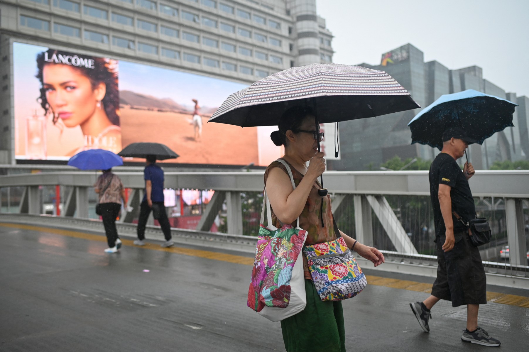Des gens portent des parapluies alors qu'ils traversent un viaduc par une journée pluvieuse à Pékin le 13 juillet 2023. (Photo par WANG ZHAO / AFP)