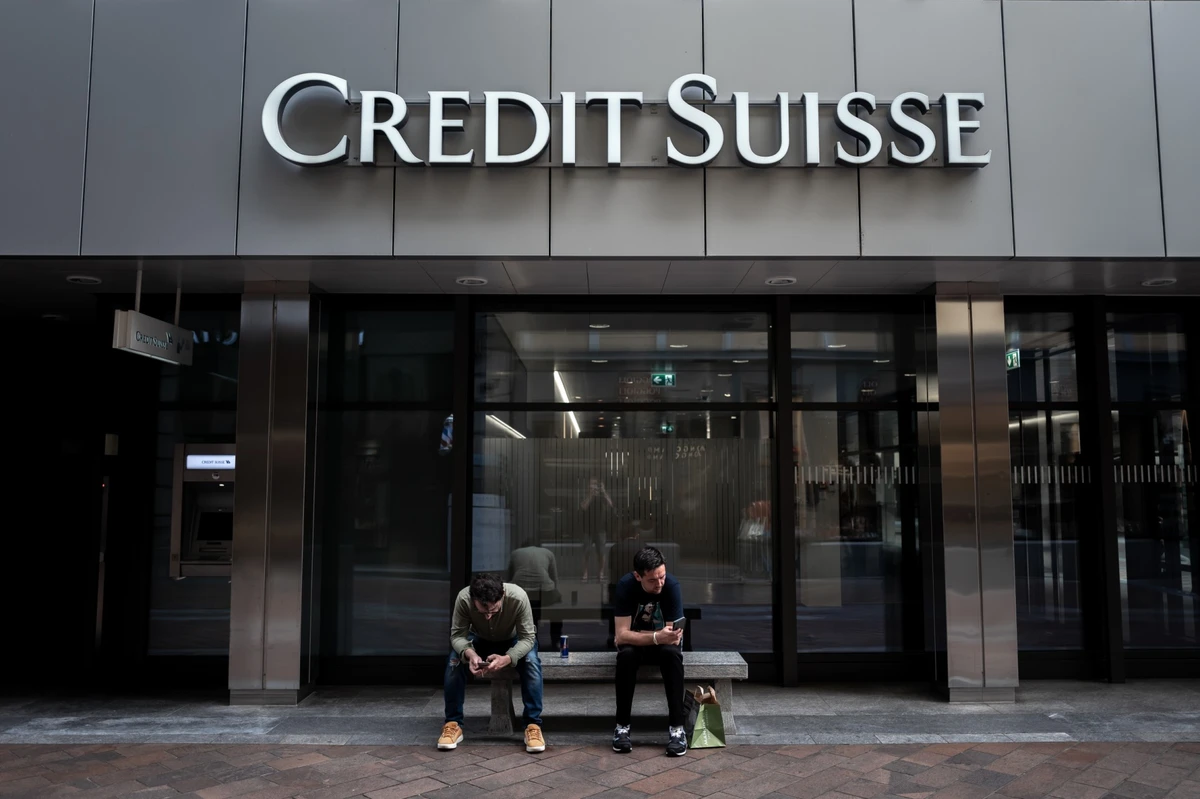Deux hommes assis sous un panneau du Credit Suisse affiché sur un bâtiment à Lugano, le 9 juin 2023. (Photo de Fabrice Coffrini / AFP)