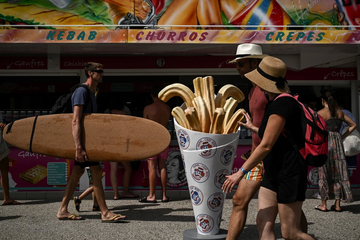 Cette photo prise le 18 juillet 2023 montre un homme tenant une planche de surf qui passe devant un marchand de glaces près d'une plage à Moliets-et-Maa, dans le sud-ouest de la France. (Photo par Philippe LOPEZ / AFP)