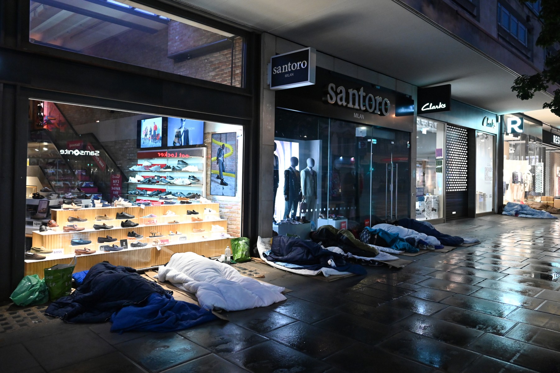 Des personnes dorment dans la rue devant des magasins fermés d'Oxford Street, aux premières heures du matin, sous la pluie, à Londres, le 2 août 2023. (Photo by JUSTIN TALLIS / AFP)