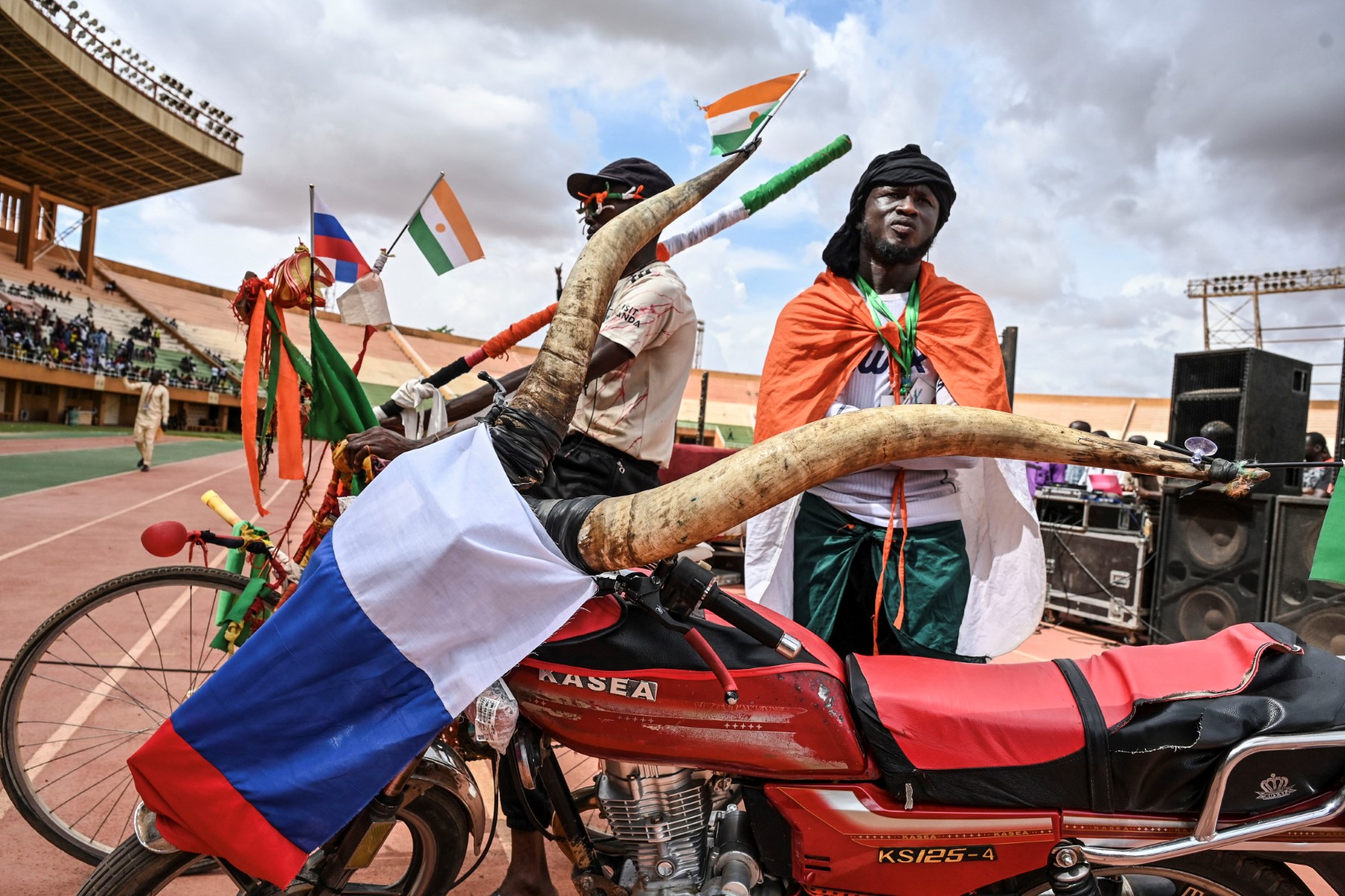Des supporters se tiennent à côté d'une moto ornée de cornes de zébu et d'un drapeau russe lors d'un concert de soutien au Conseil national pour la sauvegarde de la patrie (CNSP) du Niger au stade Général Seyni Kountche de Niamey, le 13 août 2023. (Photo AFP)