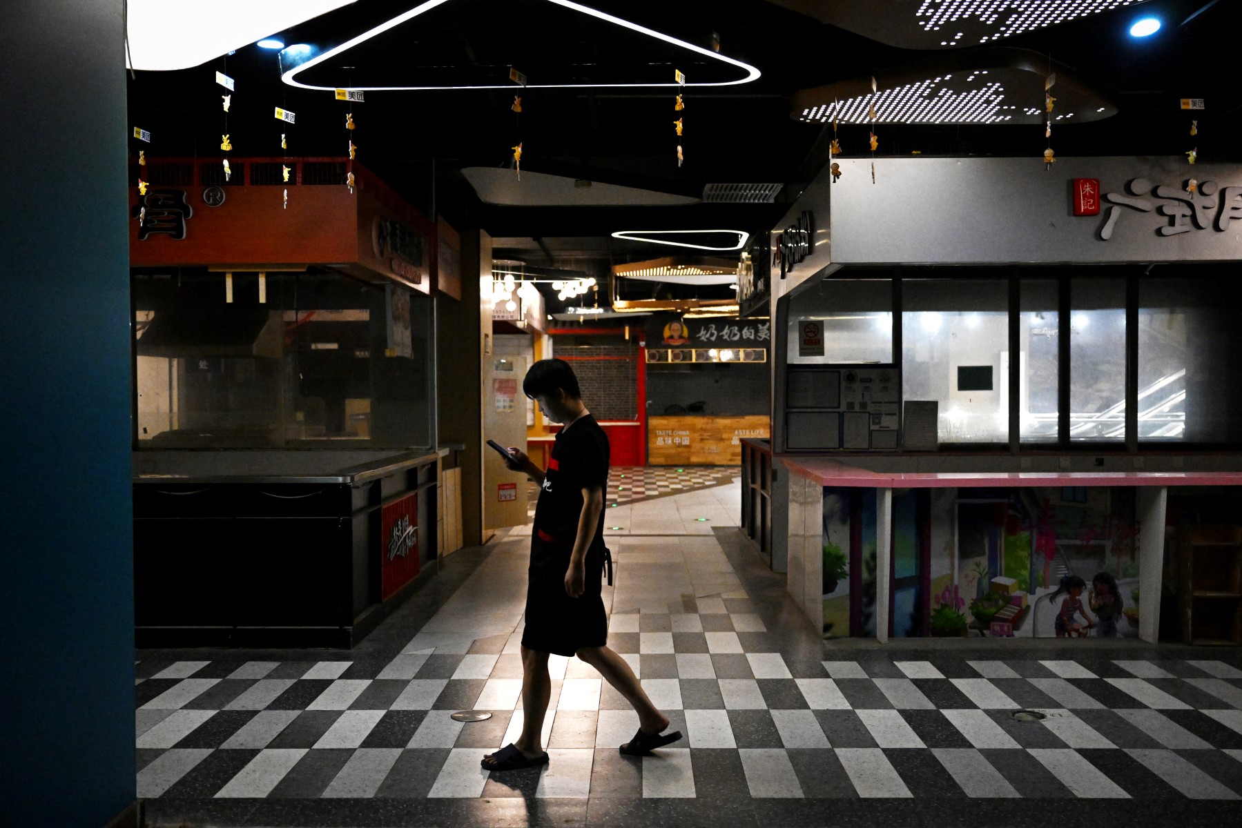 Un homme passe devant des stands de nourriture fermés dans un centre commercial à Pékin le 15 août 2023. Les actions mondiales ont chuté le 15 août, après que les données décevantes de la Chine aient renforcé les inquiétudes sur l'état de la deuxième plus grande économie du monde. (Photo par Greg Baker / AFP)