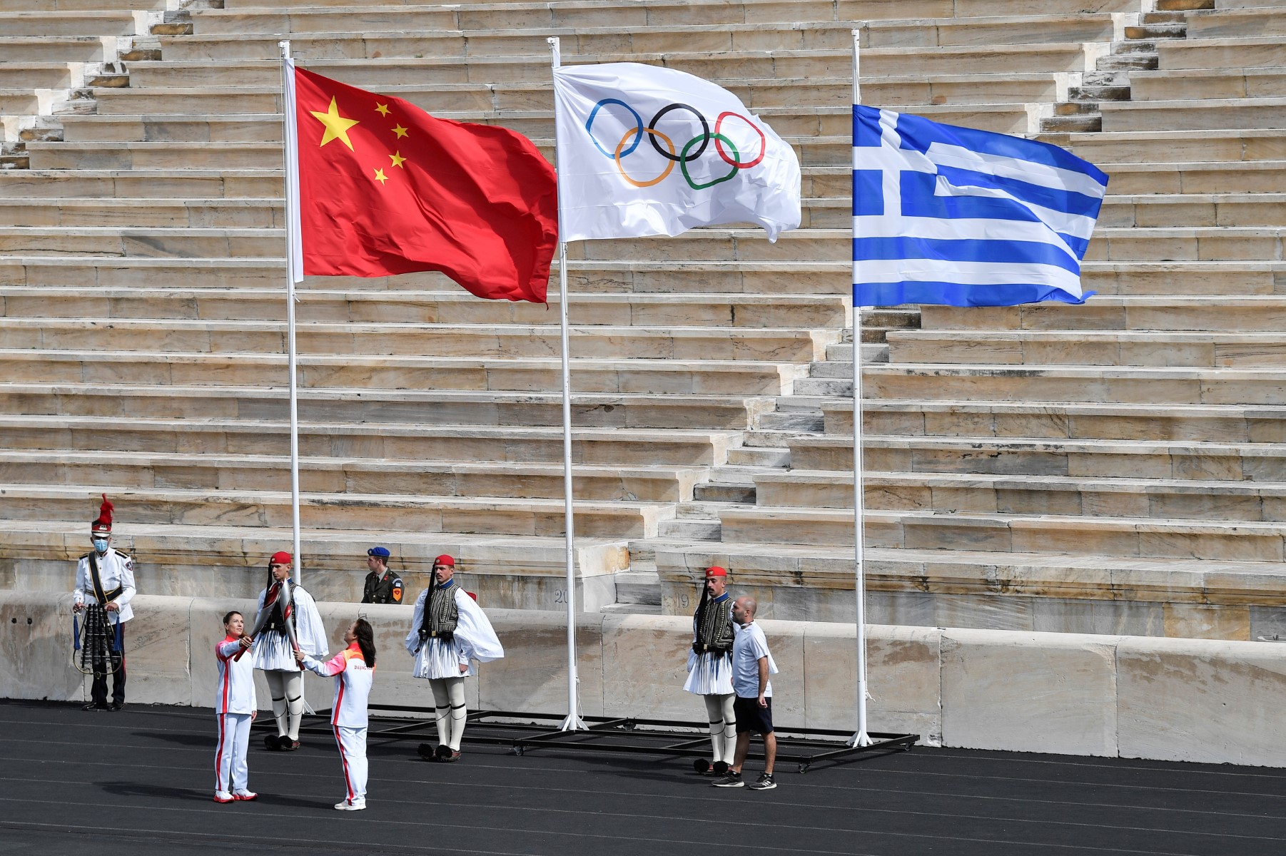 La championne olympique chinoise de ski Li Nina passe la flamme à la championne olympique grecque de ski de fond Paraskevi Ladopoulou pendant le relais de la flamme à l'intérieur du stade lors de la cérémonie de remise de la flamme olympique au stade Panathinéen d'Athènes, le 19 octobre 2021. (Photo Louisa Gouliamaki / AFP)