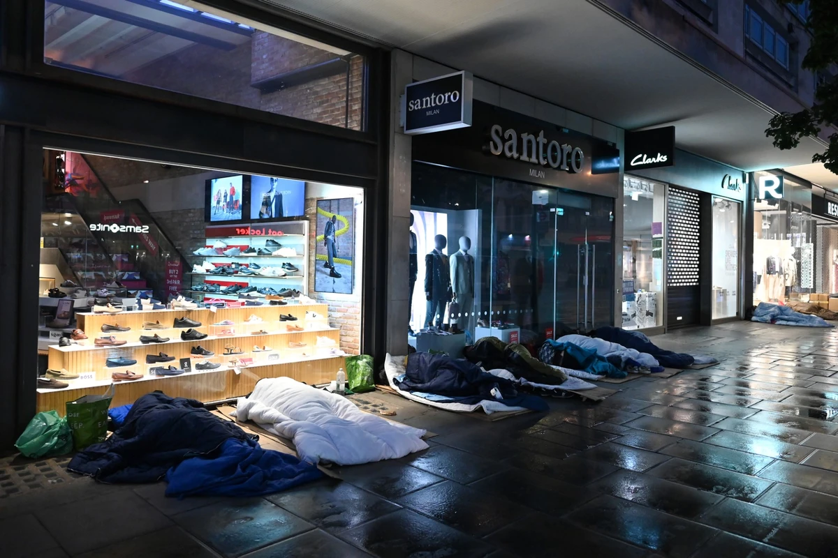 Des personnes dorment dans la rue devant des magasins fermés d'Oxford Street, aux premières heures du matin, sous la pluie, à Londres, le 2 août 2023. (Photo by JUSTIN TALLIS / AFP)