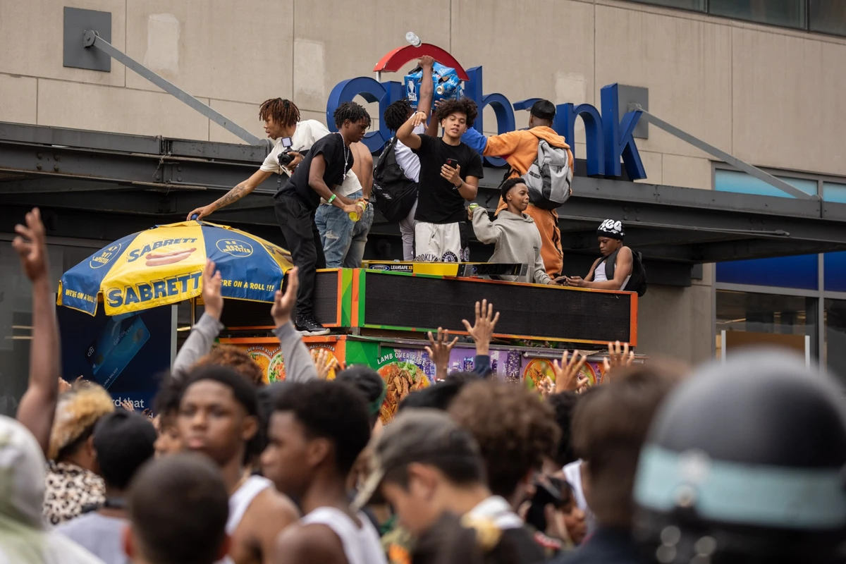 Des personnes se tiennent au-dessus du chariot d'un vendeur de rue pendant les émeutes provoquées par le streamer Twitch Kai Cenat, qui a annoncé un événement «givaway», à Union Square à New York, le 4 août 2023. (Photo Yuki Iwamura / AFP)