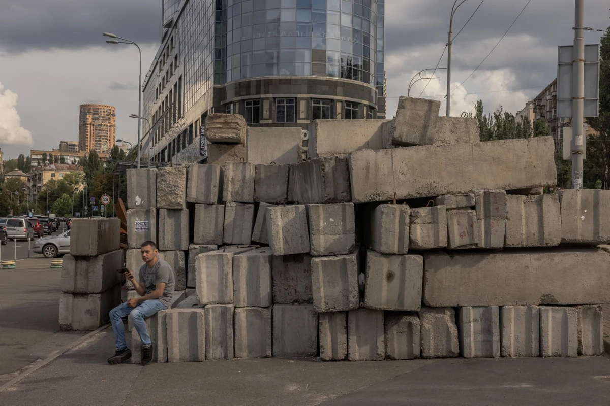 Un homme est assis à côté de blocs de béton, collectés aux postes de contrôle militaires, dans le centre de Kiev, le 2 août 2023, au milieu de l'invasion russe de l'Ukraine. (Photo par Roman PILIPEY / AFP)