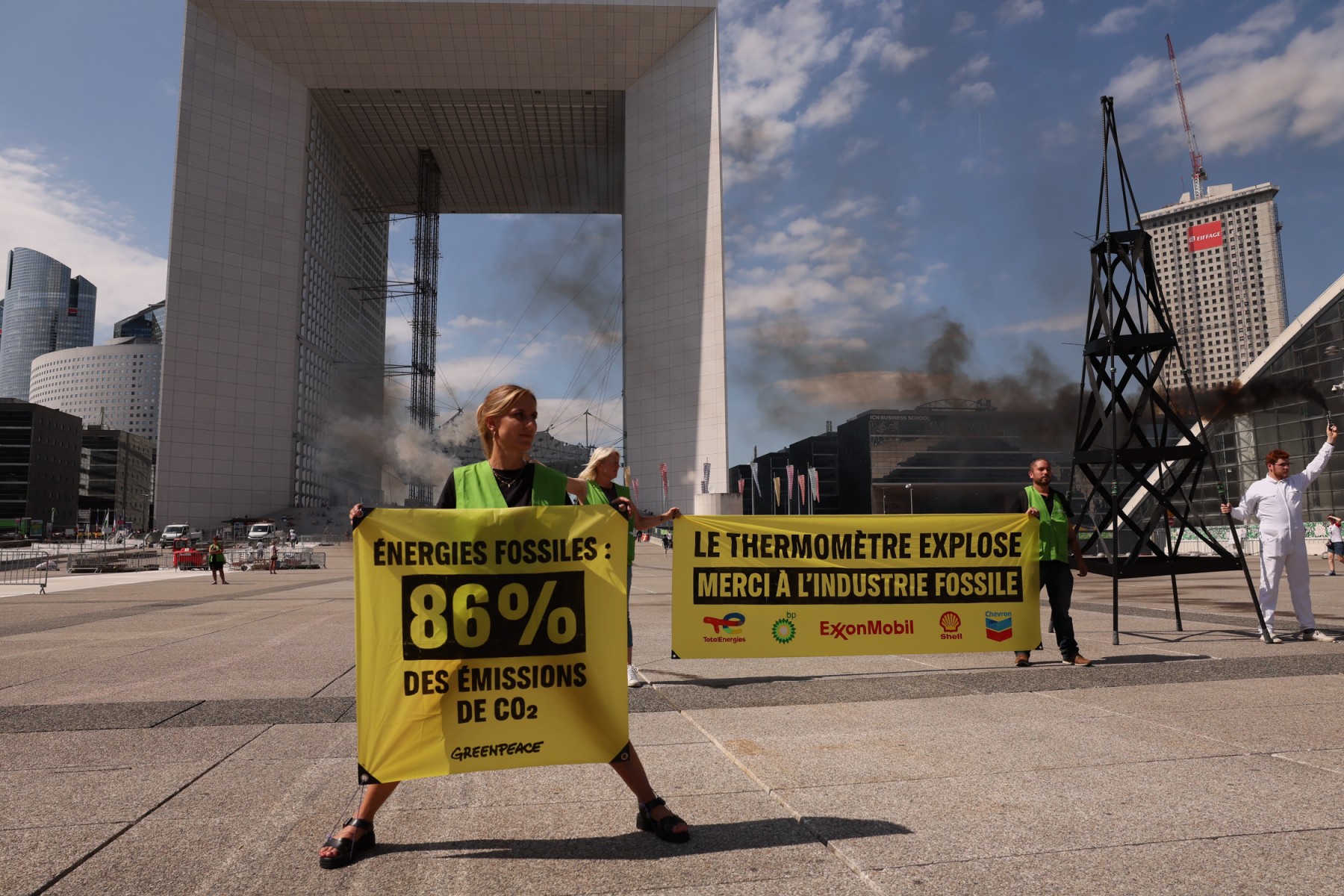 Des membres de l'ONG Greenpeace tiennent des banderoles sur lesquelles on peut lire "Les énergies fossiles : 86% des émissions de CO2" et "Le thermomètre grimpe, grâce à l'industrie des énergies fossiles" lors d'une manifestation contre l'exploitation des énergies fossiles, à La Défense, près de Paris, le 22 août 2023. (Photo Alain JOCARD / AFP)
