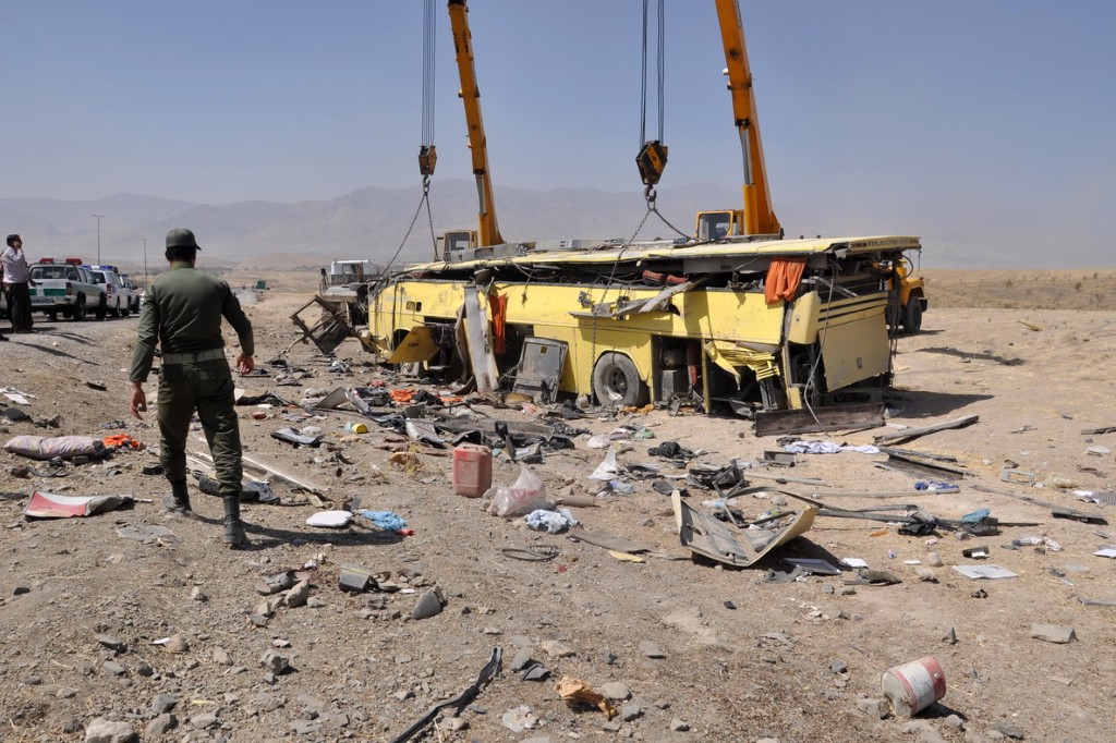 Un soldat iranien passe devant l'épave d'un bus sur la route reliant Arak à Borujerd, dans l'ouest de l'Iran, le 17 septembre 2013. (Photo Adel Azizi / ISNA NEWS AGENCY / AFP)