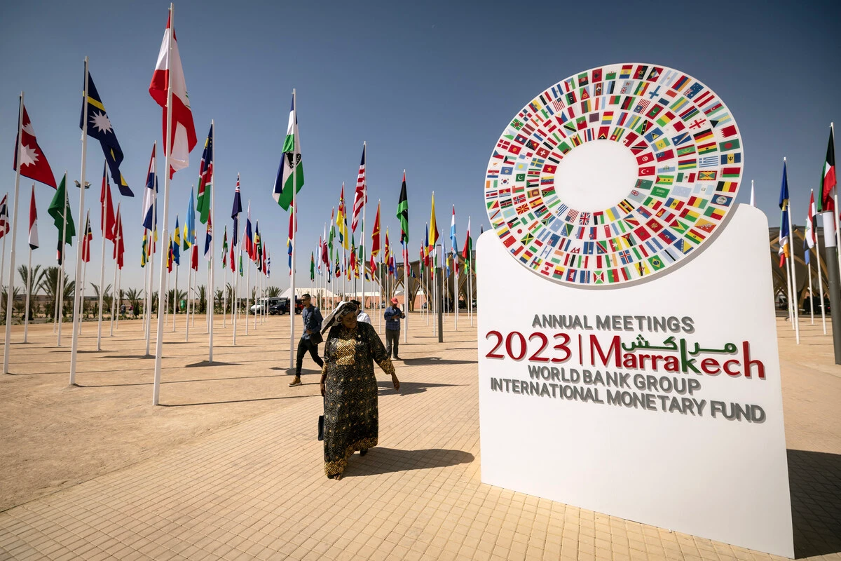 Une femme passe devant l'emblème des réunions annuelles du FMI et de la Banque mondiale de 2023 situé à l'entrée du site à Marrakech, le 8 octobre 2023. (Photo FADEL SENNA / AFP)