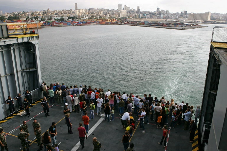 Des ressortissants étrangers observent Beyrouth à bord du navire de guerre français "Mistral" alors qu'ils fuient le Liban déchiré par la guerre, le 10 août 2006, pour se rendre sur l'île méditerranéenne de Chypre. (Photo by Nicolas Asfouri AFP)