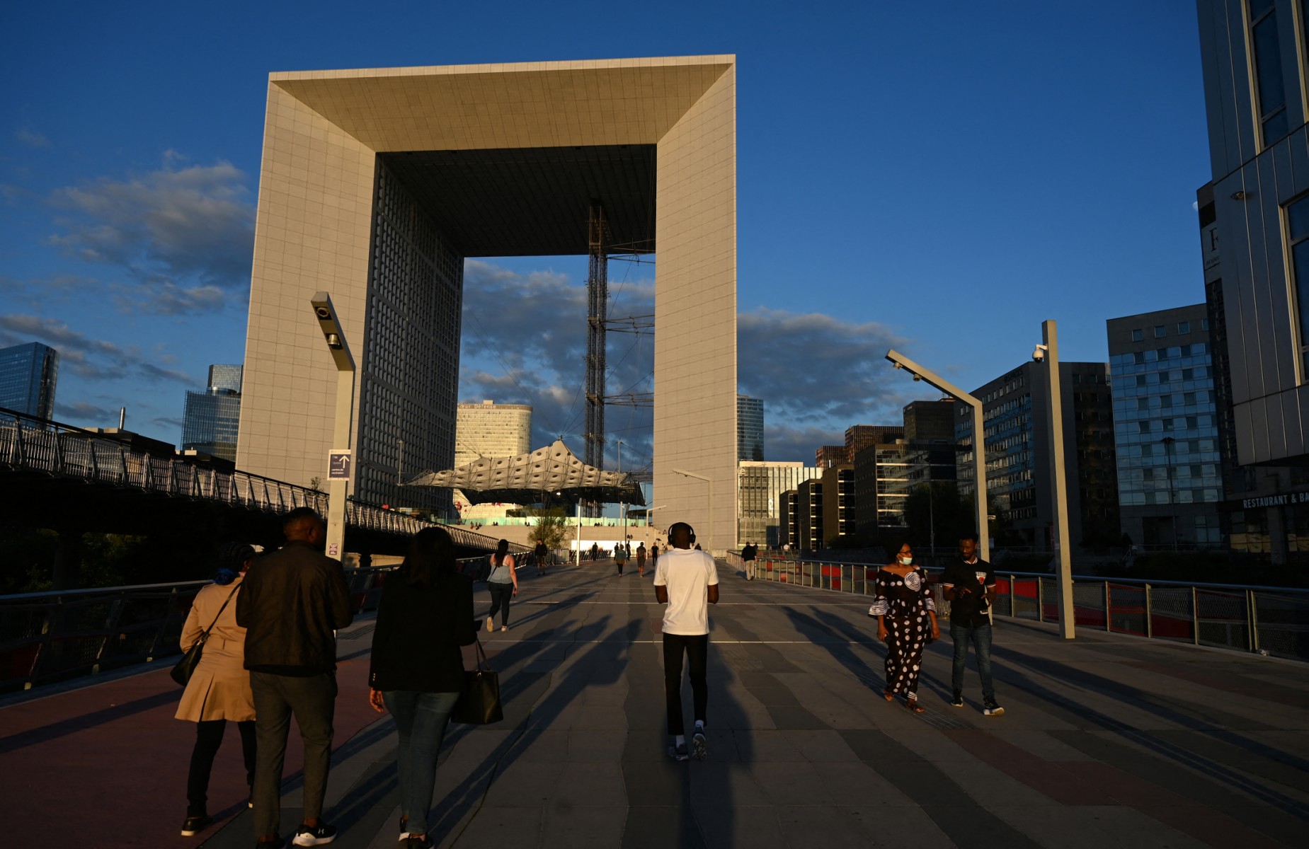 Des personnes marchent devant la Grande Arche de la Défense dans le quartier d'affaires de la Défense, dans la banlieue ouest de Paris, à Puteaux, le 16 juin 2022. (Photo Emmanuel DUNAND / AFP)