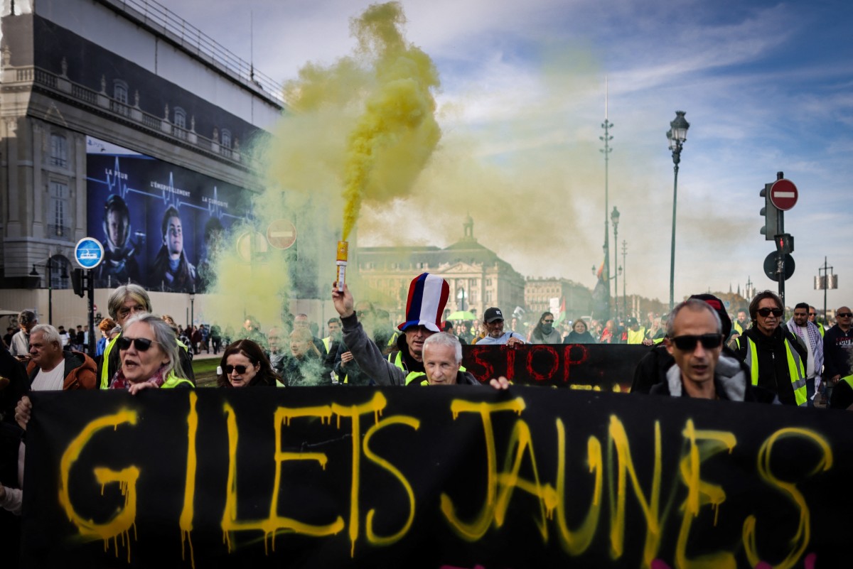 Des manifestants, portant des gilets jaunes, tiennent une fusée éclairante et une banderole indiquant "Gilets jaunes, nous sommes là" lors d'un rassemblement marquant le 5e anniversaire des manifestations antigouvernementales dites "Gilets jaunes" en 2018-2019, à Bordeaux, en France, le 18 novembre 2023. (Photo Thibaud Moritz AFP)